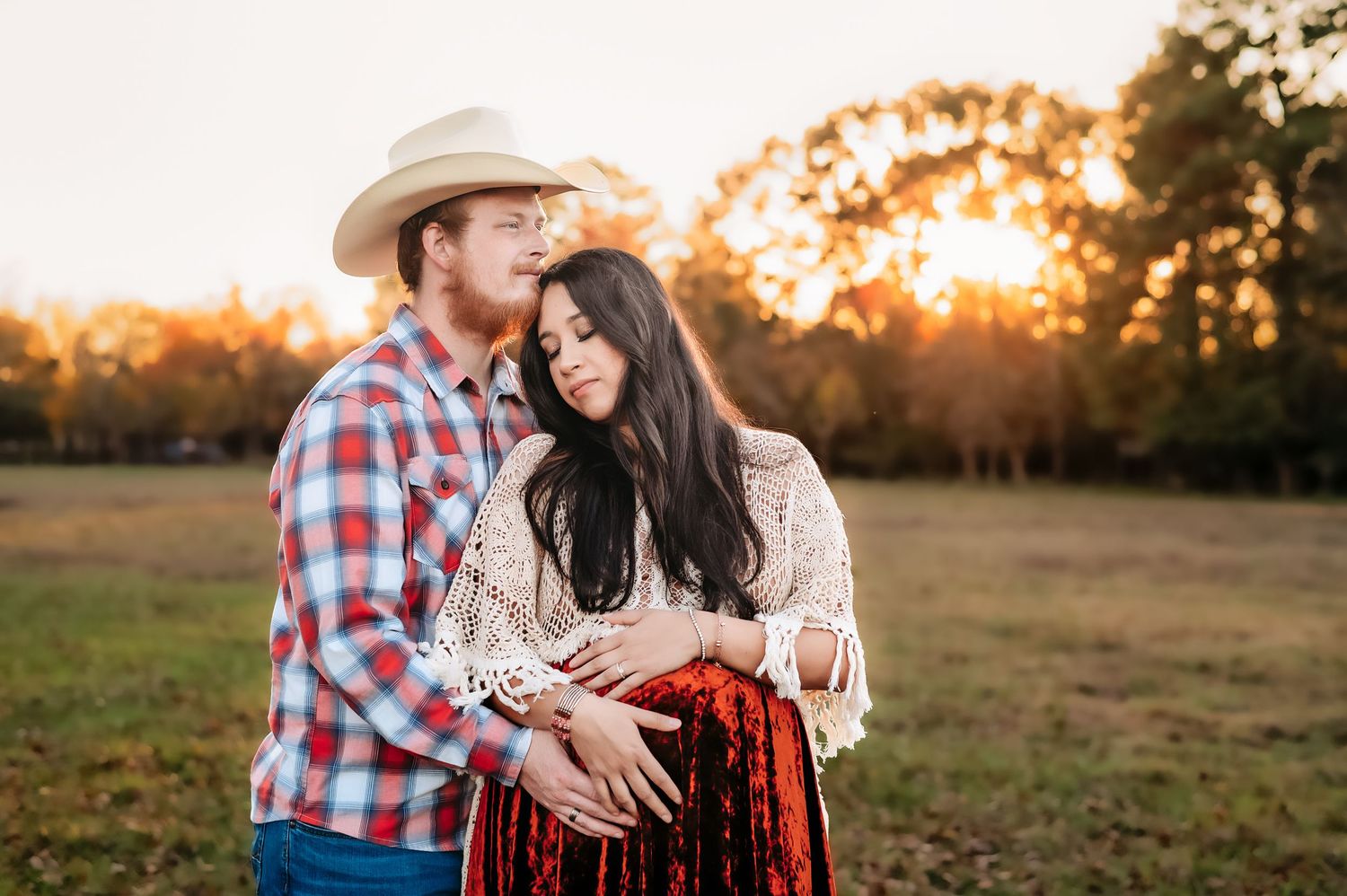 A romantic sunset maternity photo with a couple embracing in front of golden light.