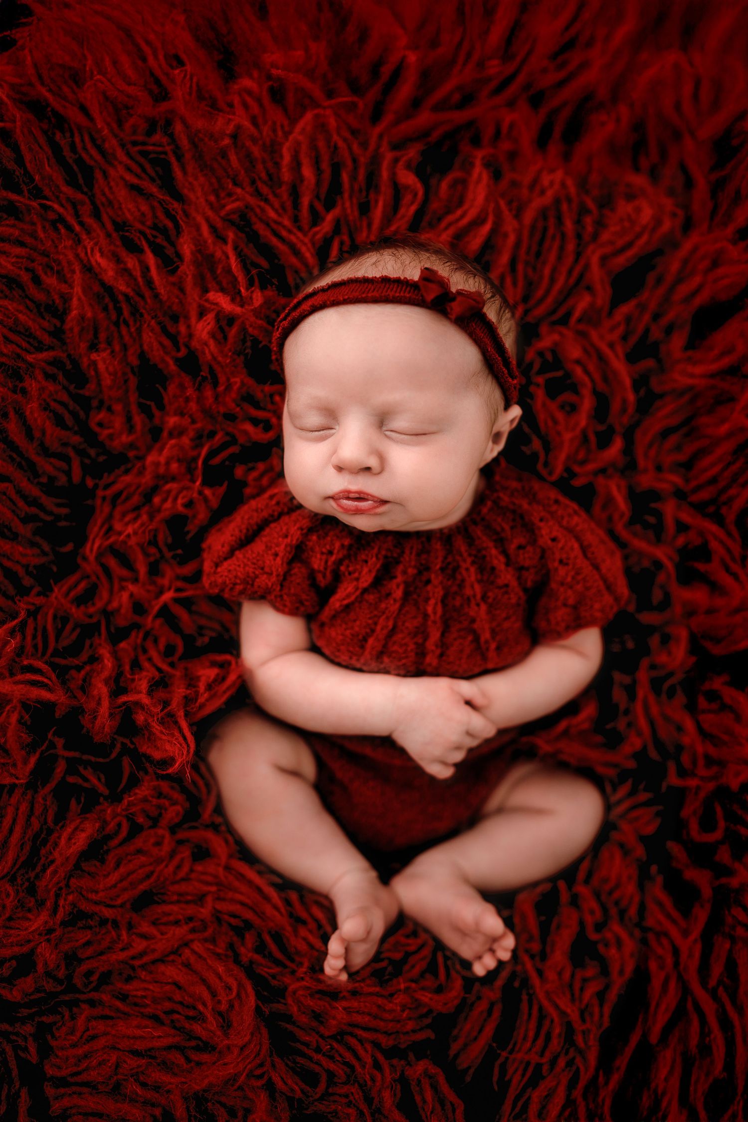 Sleeping newborn baby nestled in soft red textured blanket photographed from different angles.