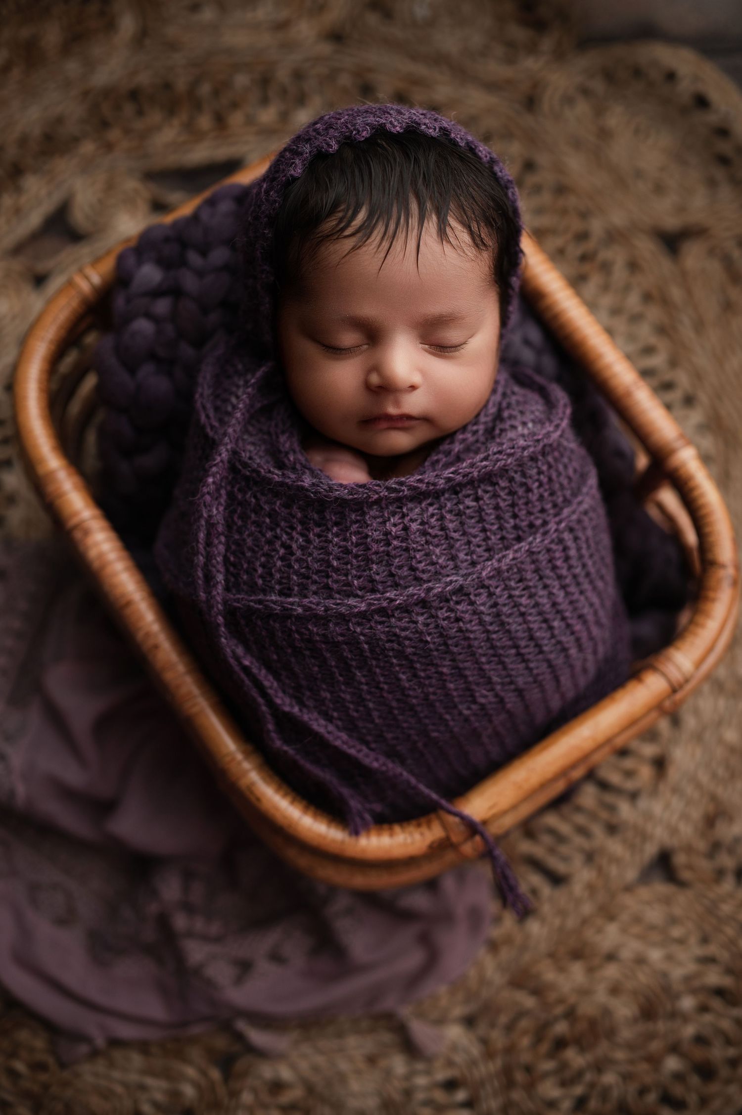 Sleeping baby nestled in a cozy purple knit blanket inside a small woven basket.