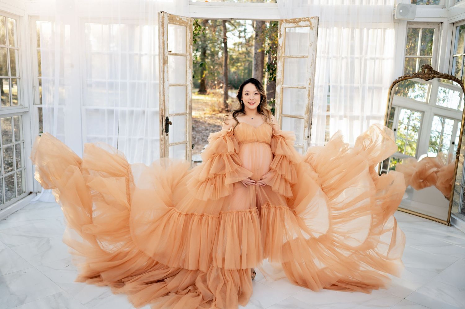 A flowing peach-colored tulle gown with dramatic ruffles fills an elegant room with French doors and mirrors.