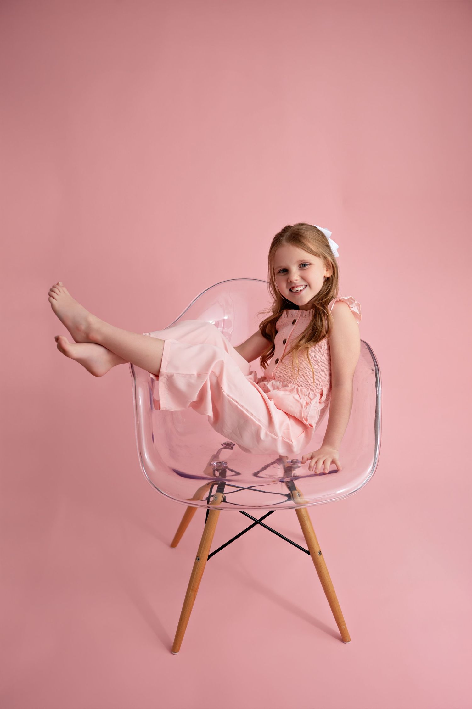 A series of playful poses on a clear acrylic chair against a pink backdrop shows movement and energy.