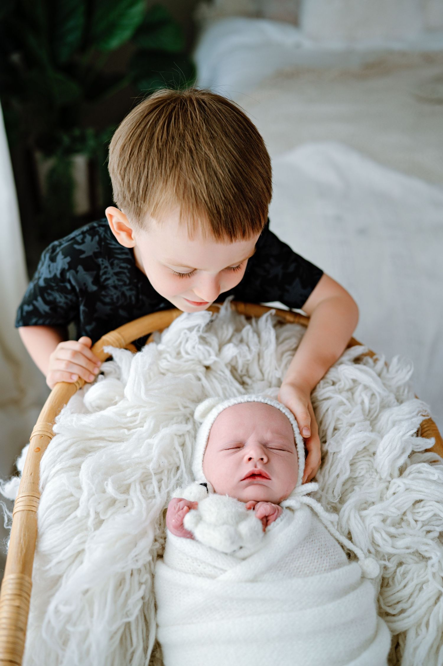 Child looking down at sleeping baby nestled in white textured bedding.