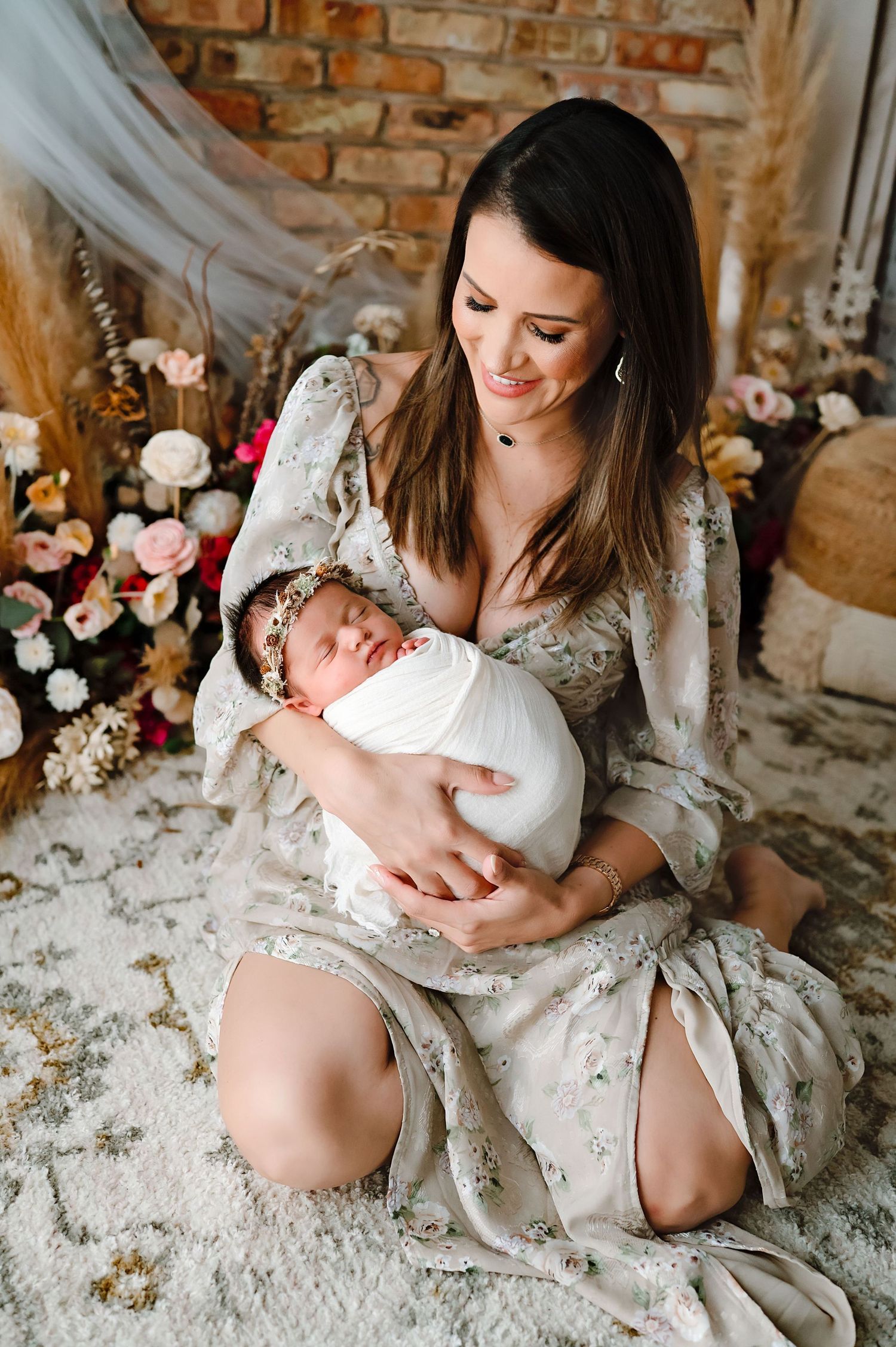 A tender moment with a newborn baby being held in a rustic setting with brick walls and floral decor.