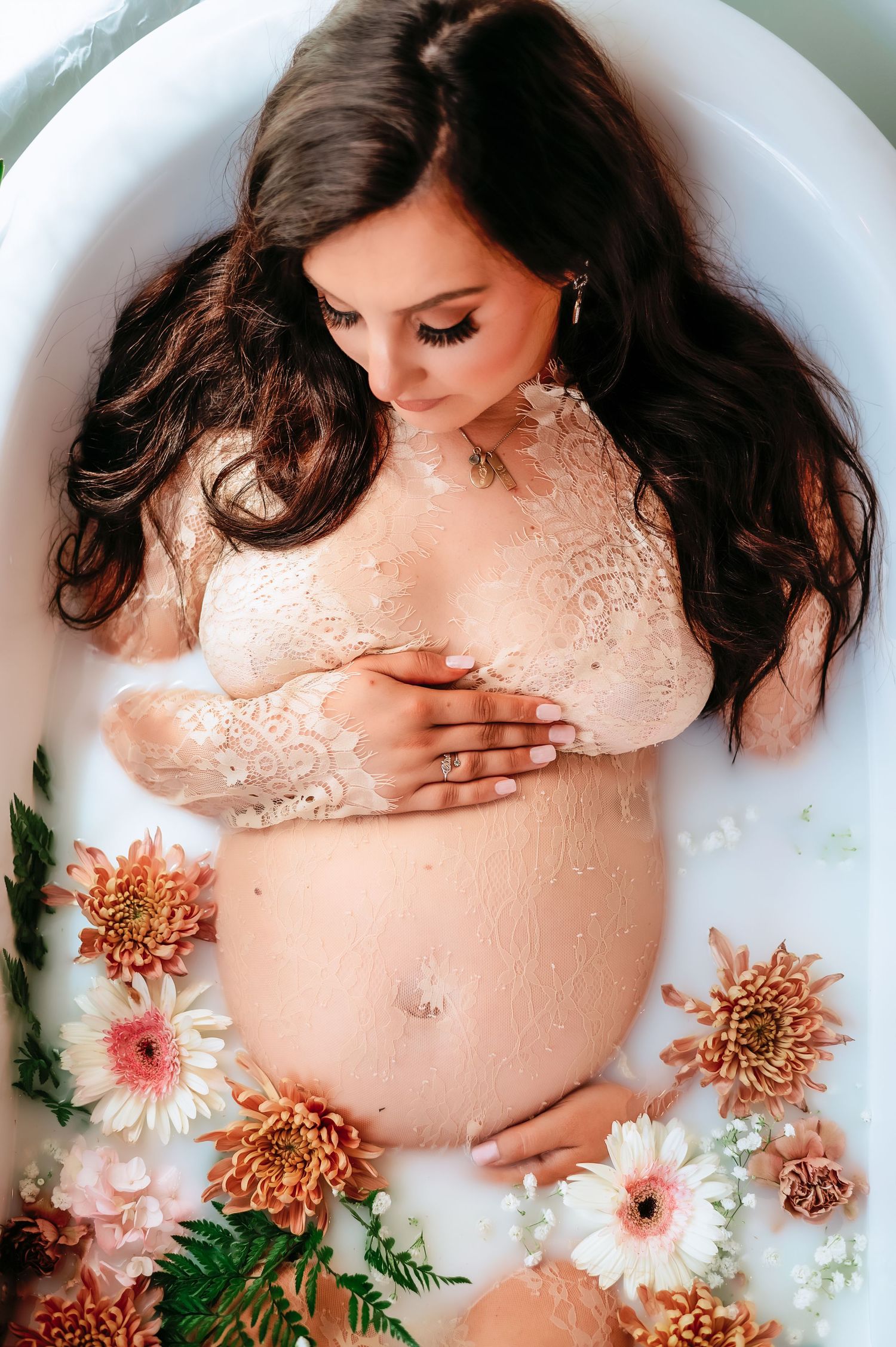 A milk bath maternity photo with pink and orange flowers surrounding an expecting mother.