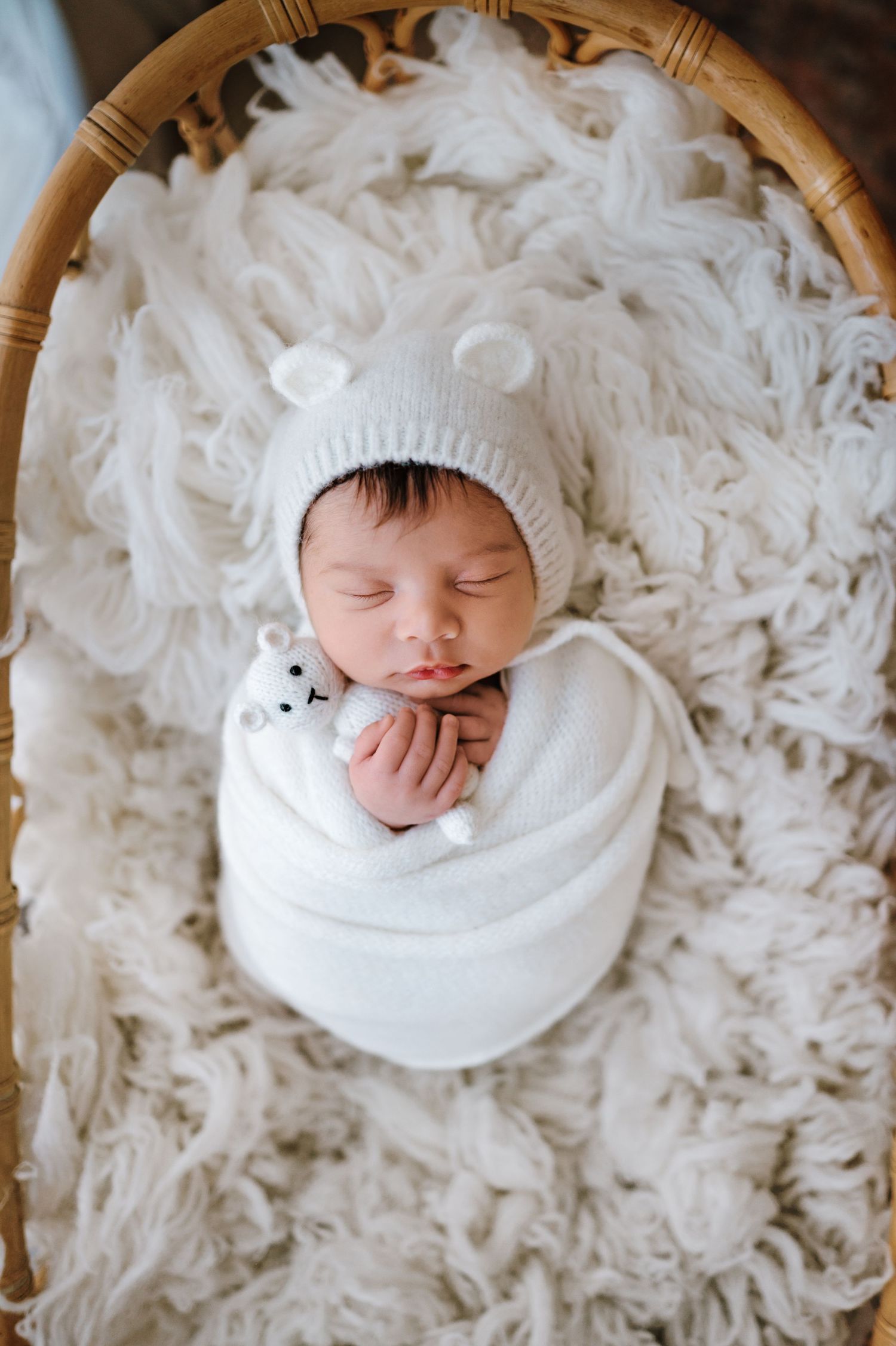 A sleeping newborn in a white knit hat lies nestled in soft white feathery bedding.