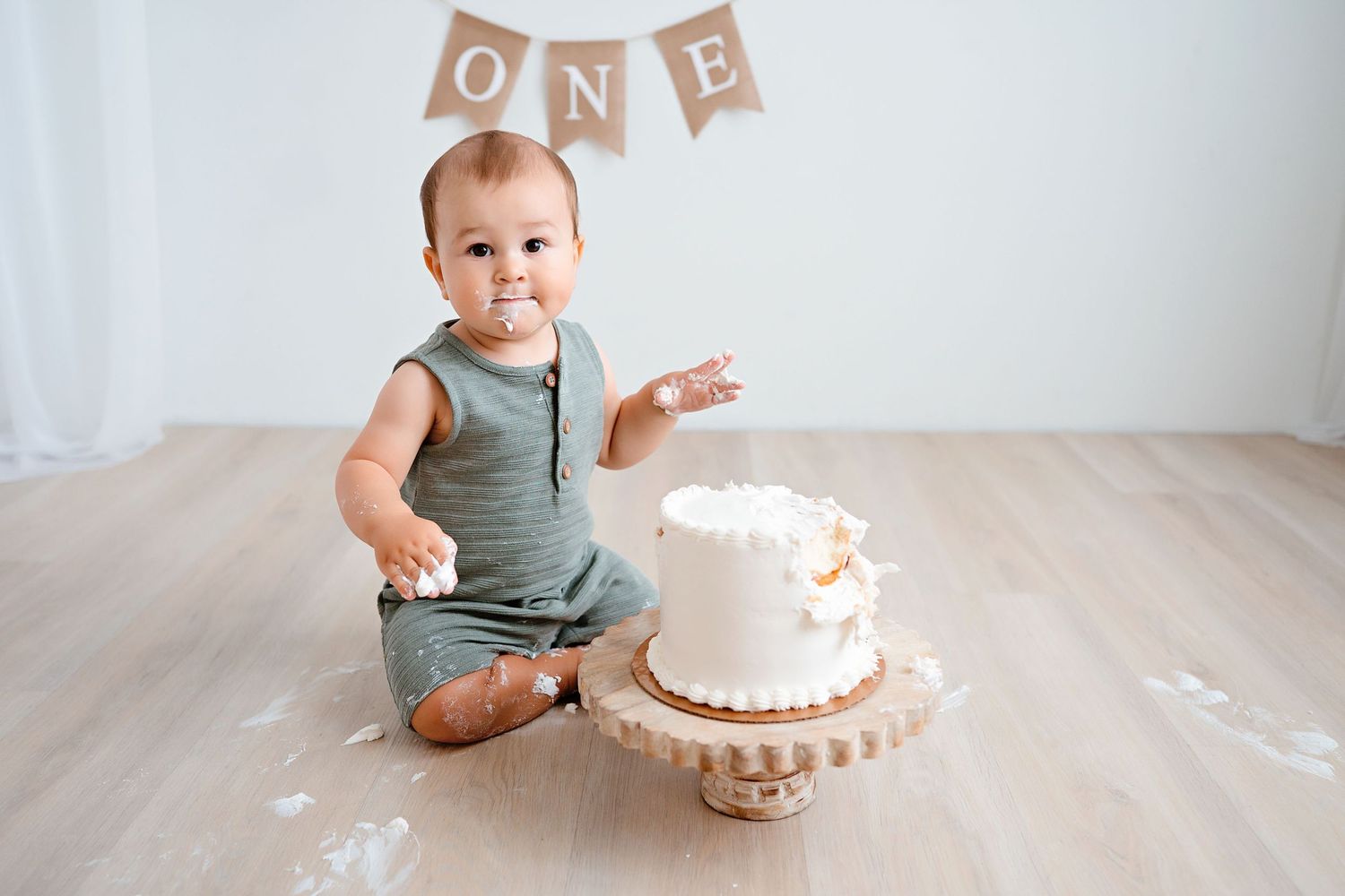 First birthday cake smash session with simple white cake and rustic wooden floor.