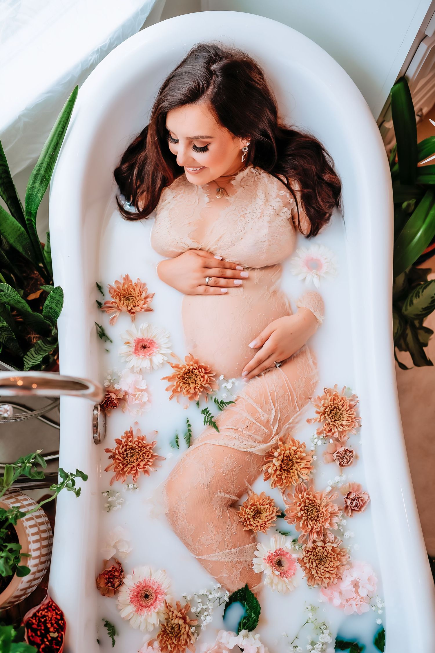 A maternity milk bath photo with orange flowers and greenery floating in white water.
