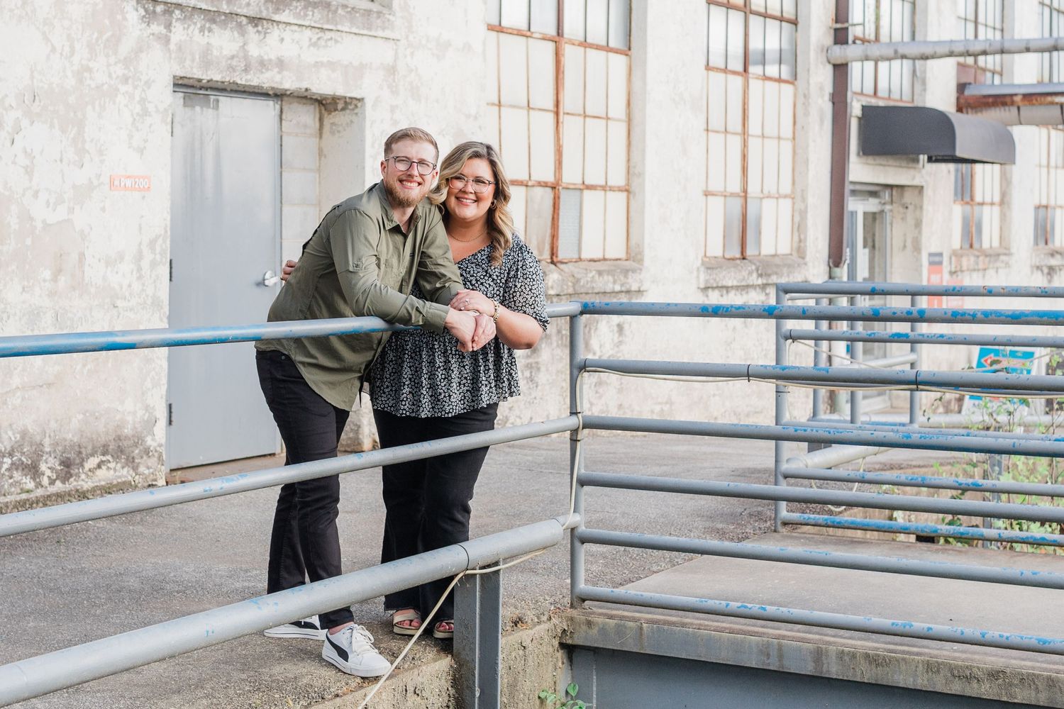 Couple standing at the entryway to Taylors Mills smiling and leaning against a metal railing.