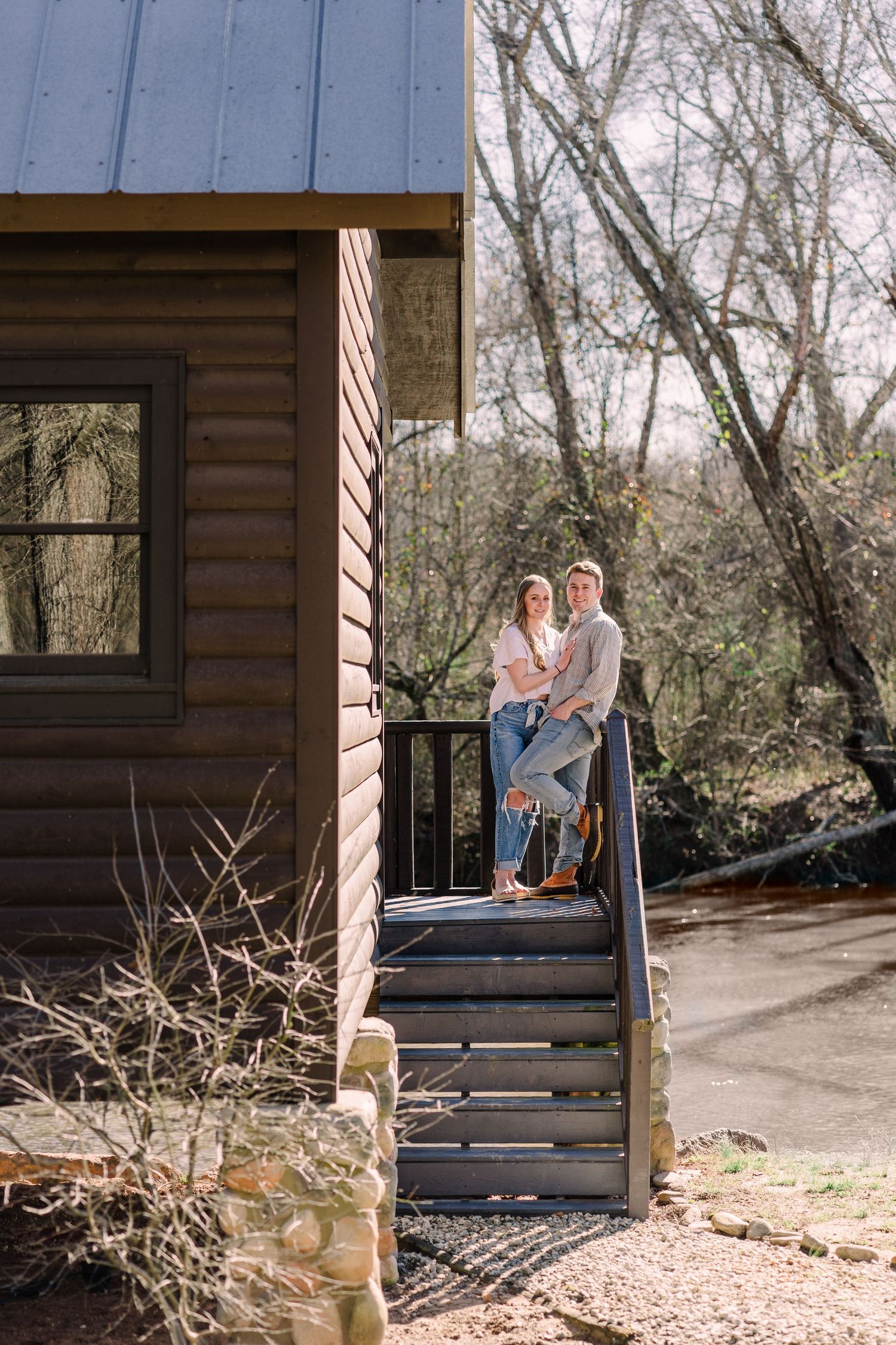 Couple smiling and leaning against a cabin railing wearing jeans and buttown down shirts.