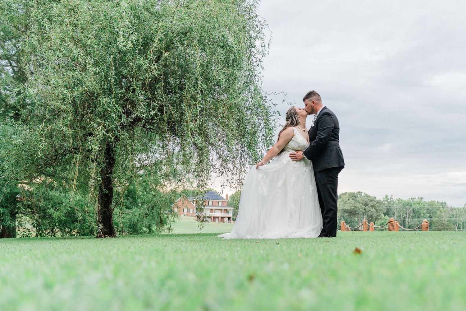 bride and groom kissing below a willow tree in front of the lake
