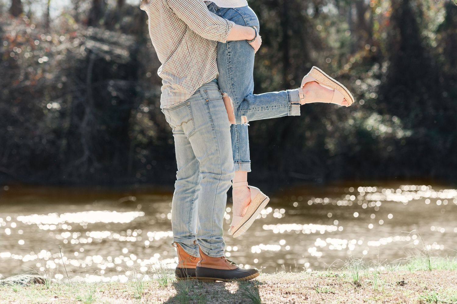 Man lifting fiancee playfully by the water's edge