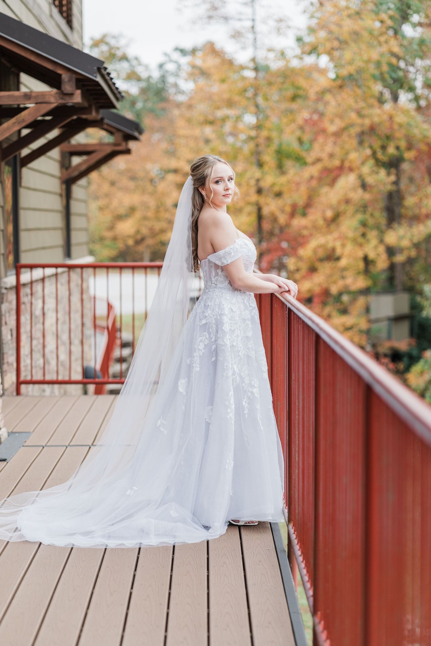 Bride leaning agains the railings and looking over her shoulder with bright yellow and red leaves behind her