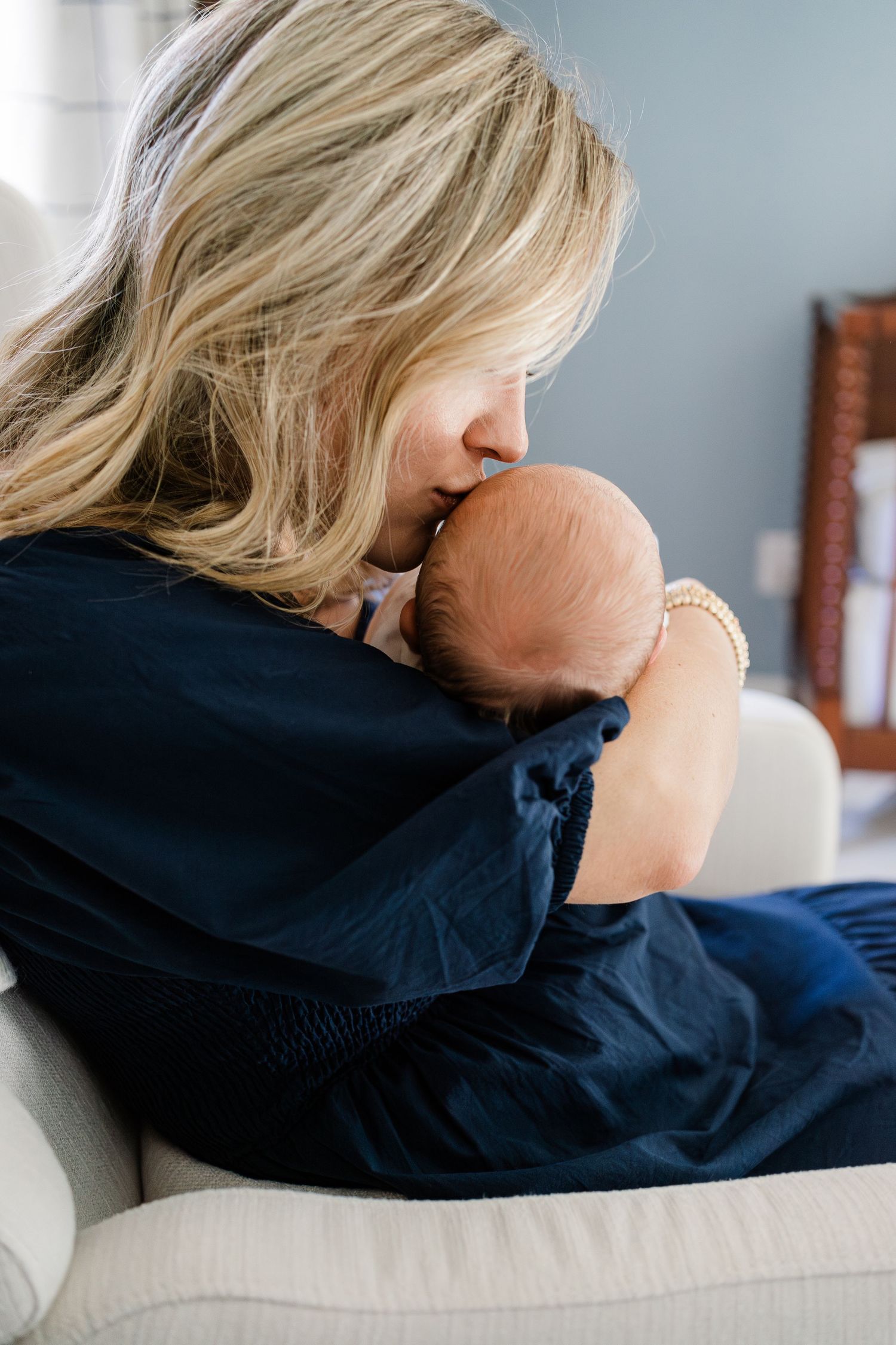 Mother cuddling newborn baby boy on nursery rocker during lifestyle photography session in Greenville SC