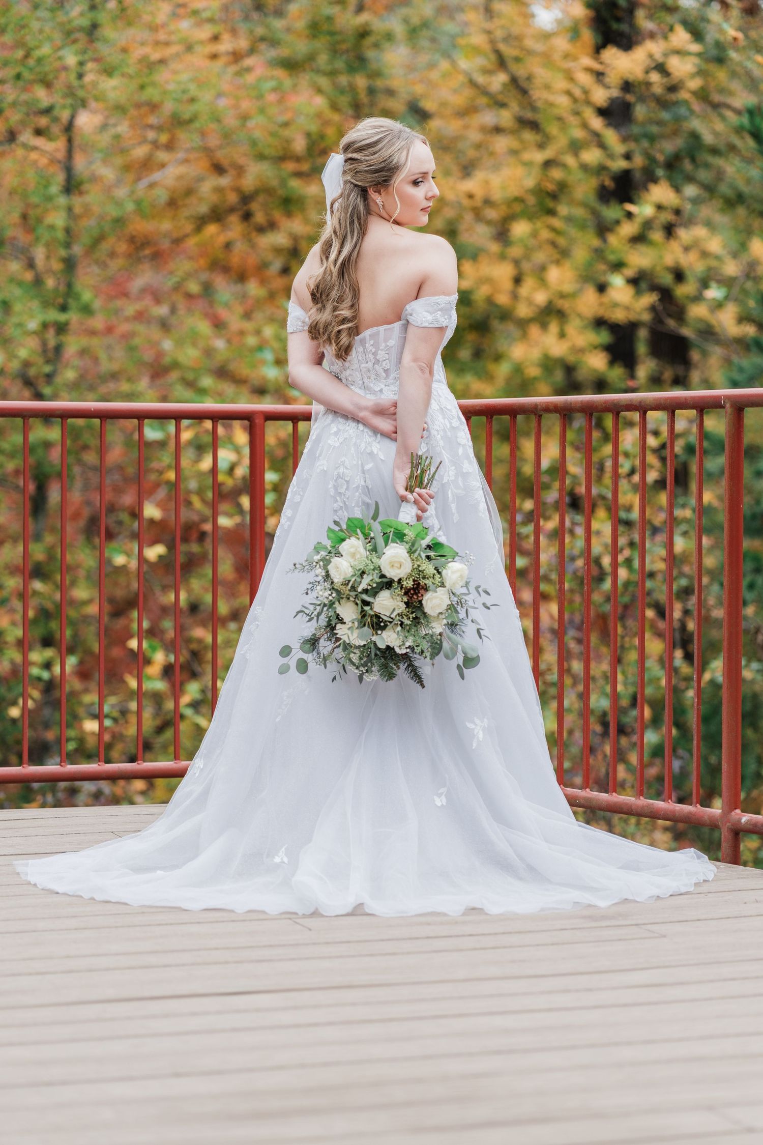 bride standing with bouquet behind her back looking out over the overlook at the fall foliage
