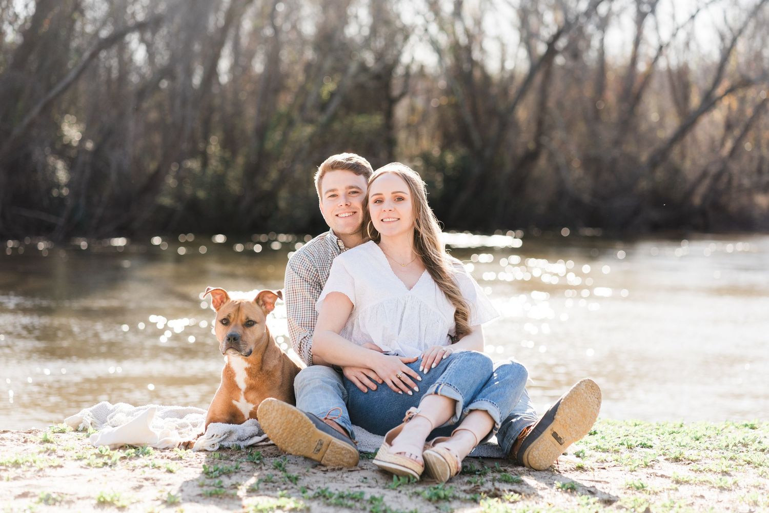 Couple sitting on a blanket by the river with their dog.