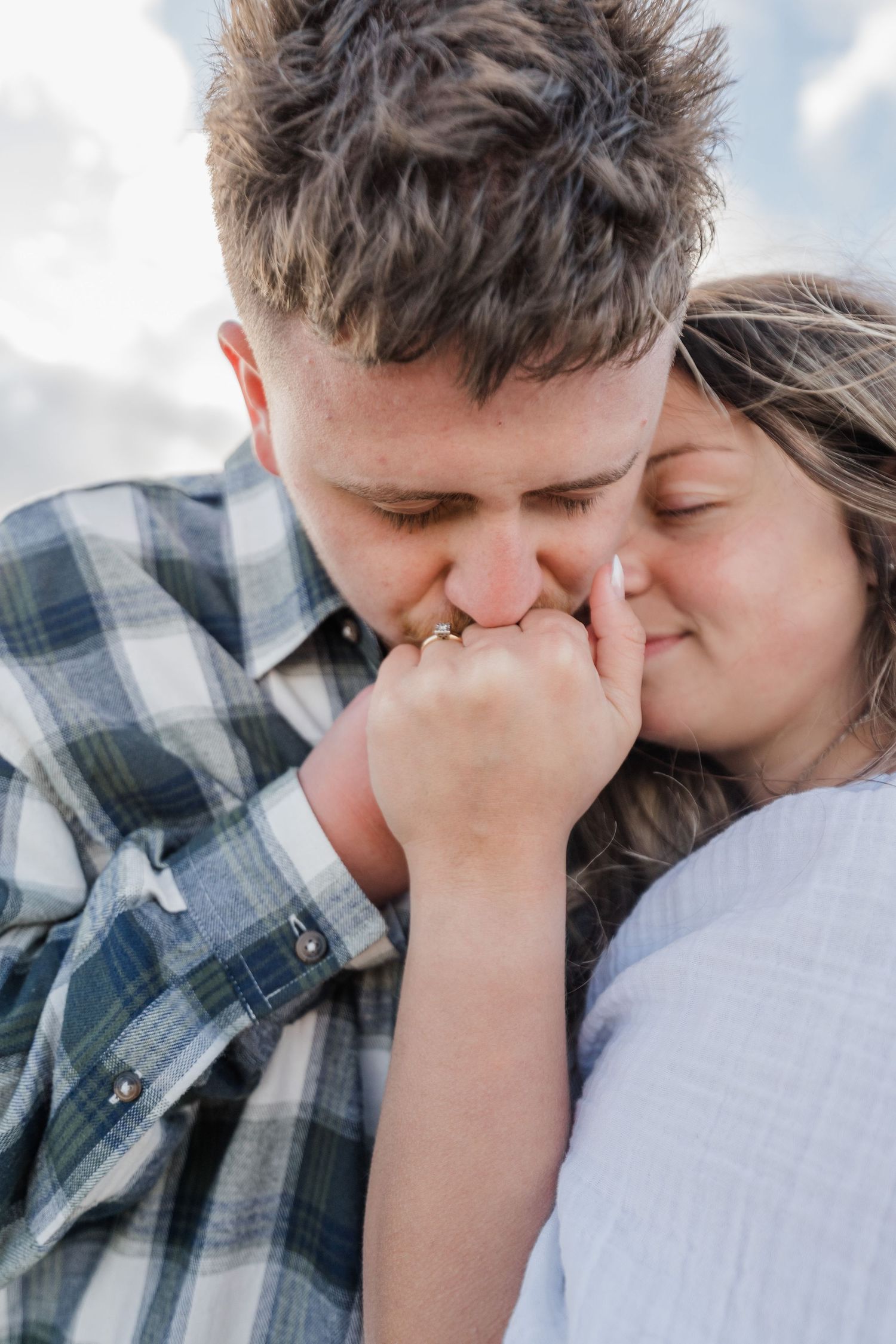 Man kisses his fiancees hand while she closes her eyes and lays her head on her shoulder