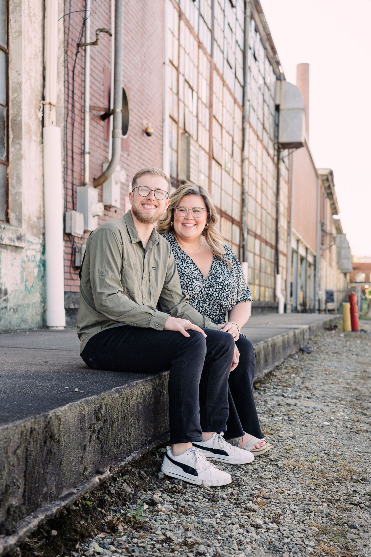 Couple sitting on the sidewalk in front of Taylors Mill, smiling at the camera