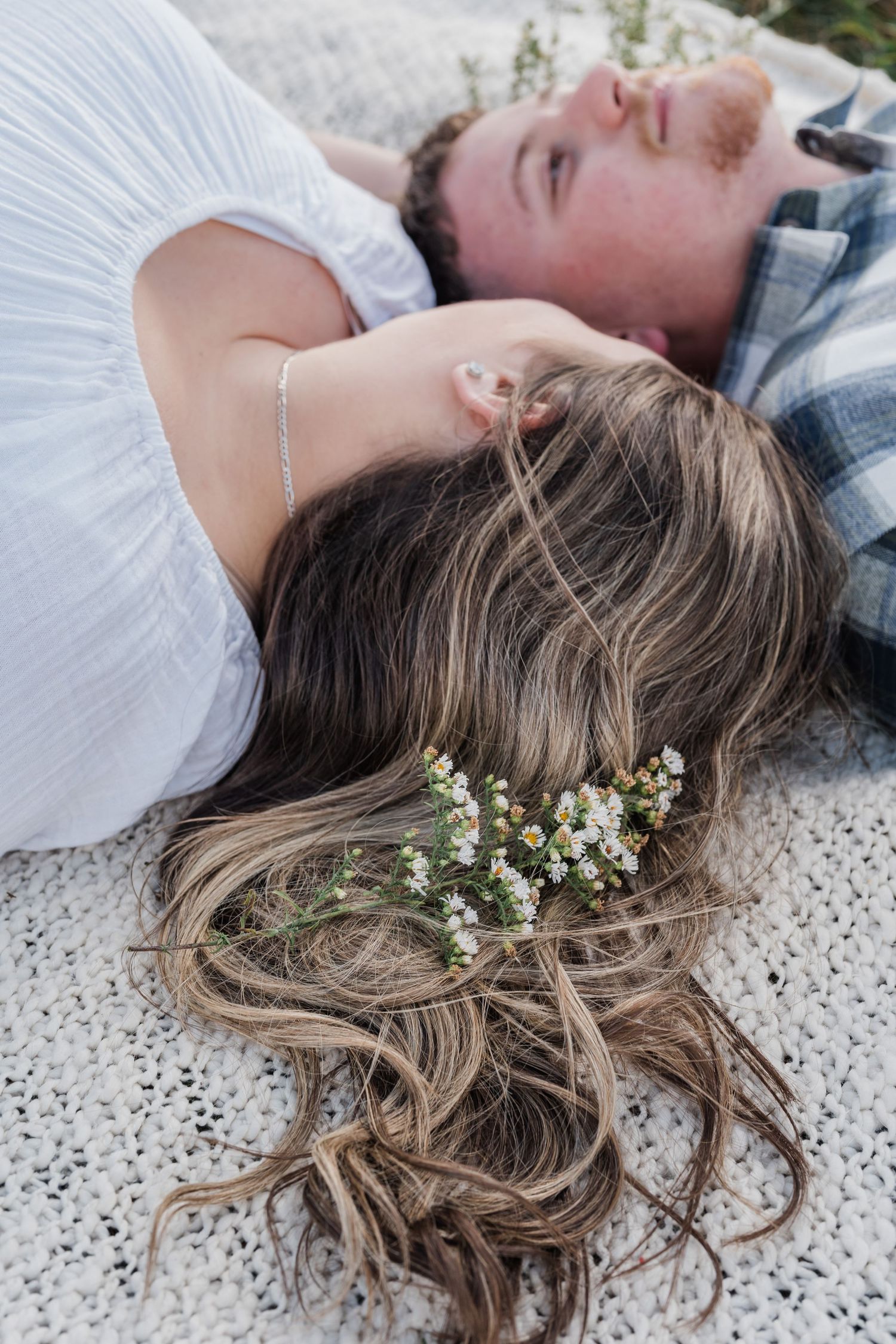Man and woman lying down on a blanket together, with flowers in the woman's hair.