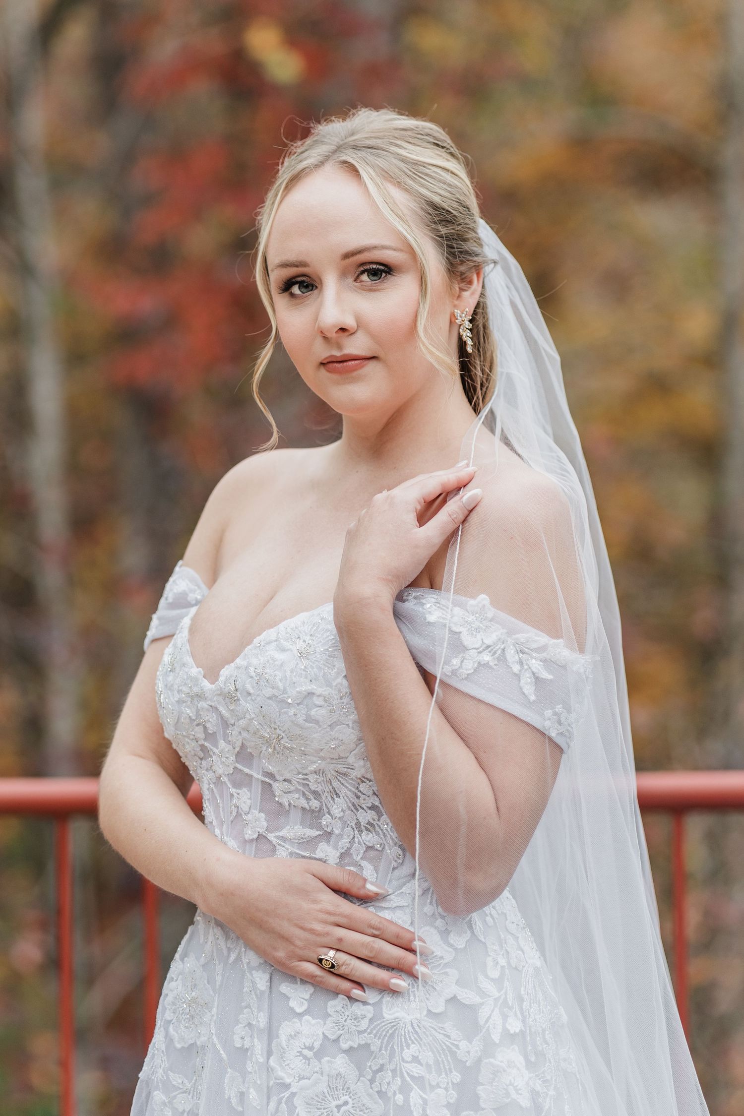 Bride posing with her hand on her shoulder with vibrant leaves in the background