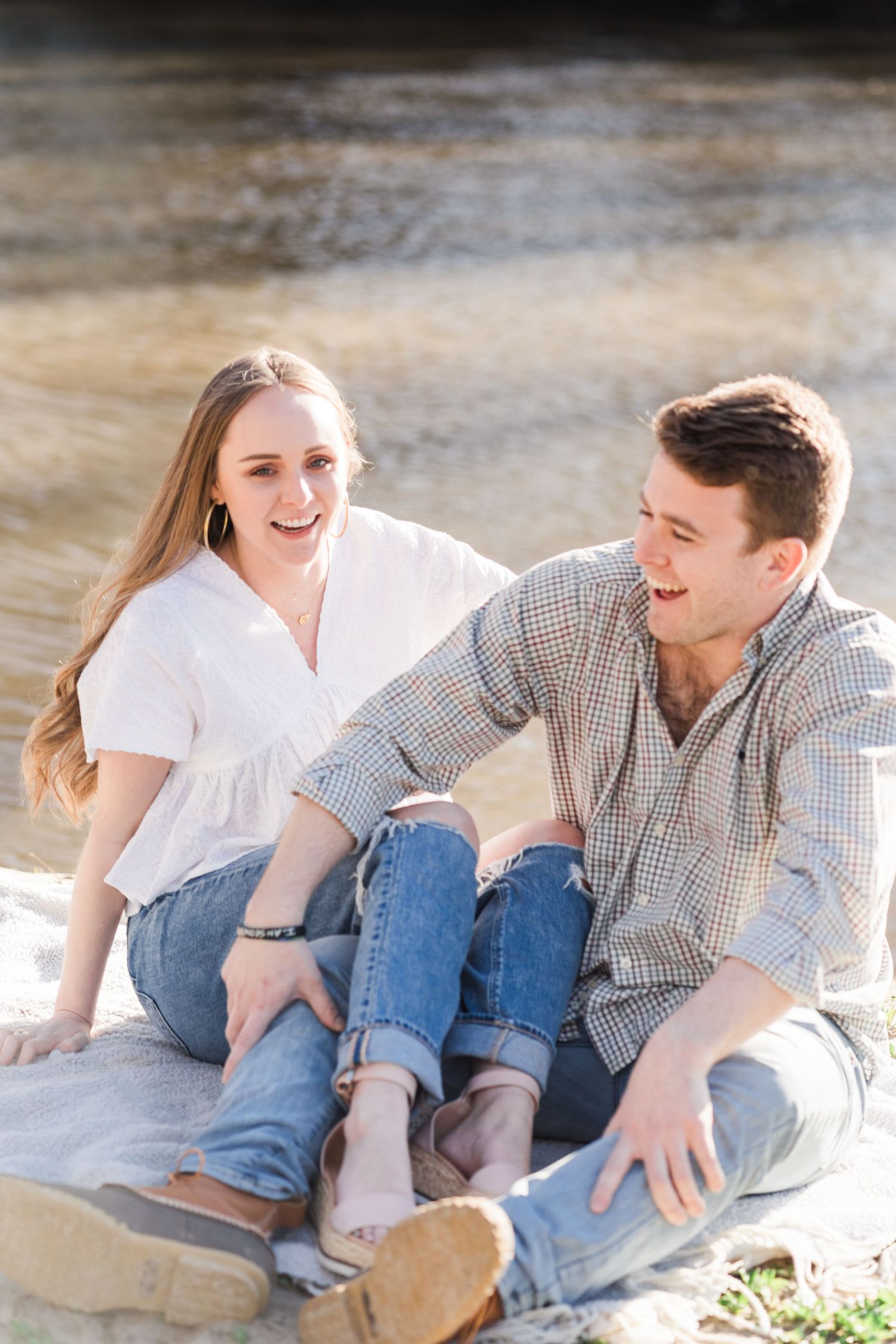 Man and woman sitting on a blanket by the river, laughing together