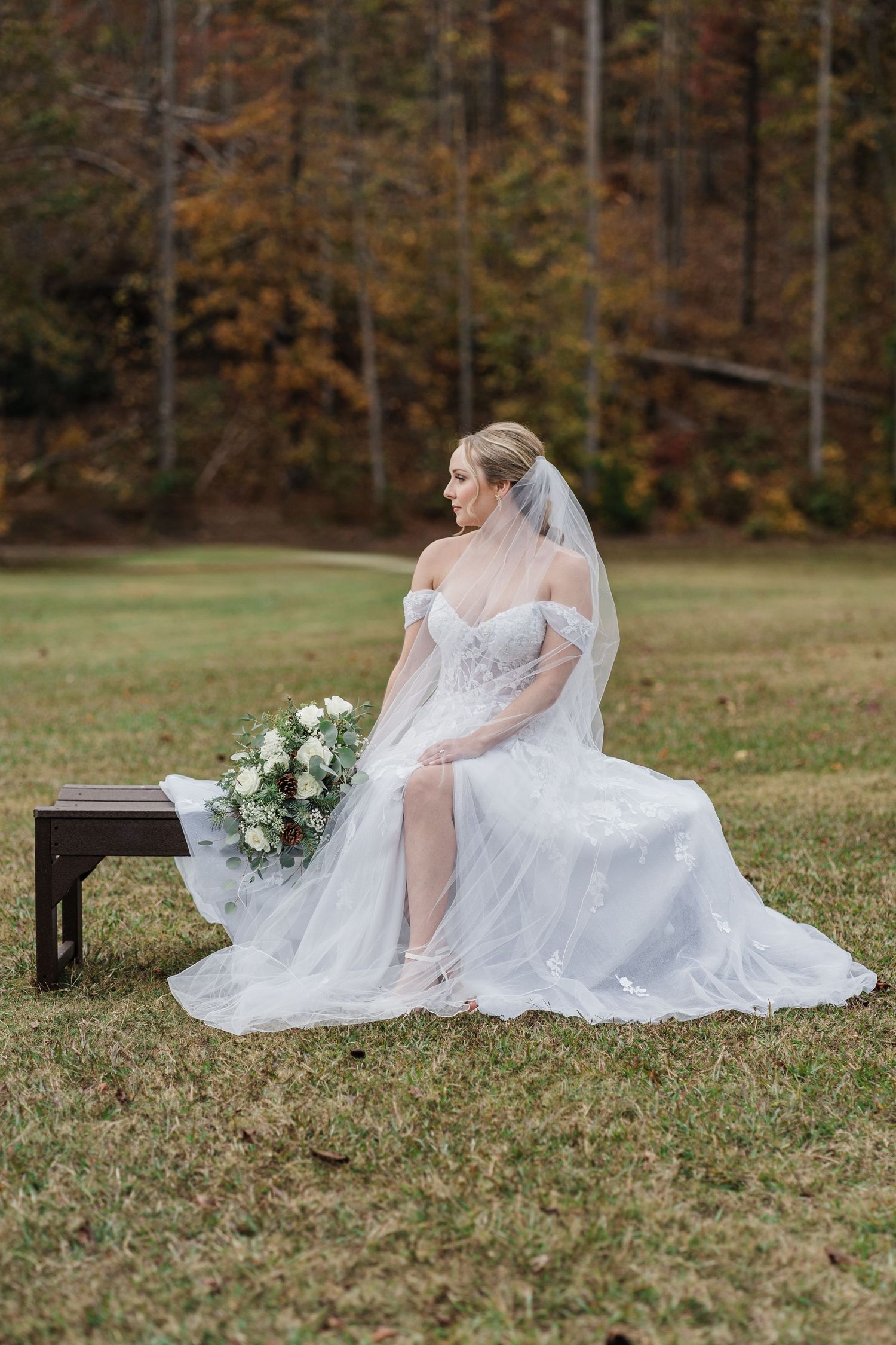 bride wearing her gown and veil while sitting on a bench in the middle of a field at Camp Spearhead