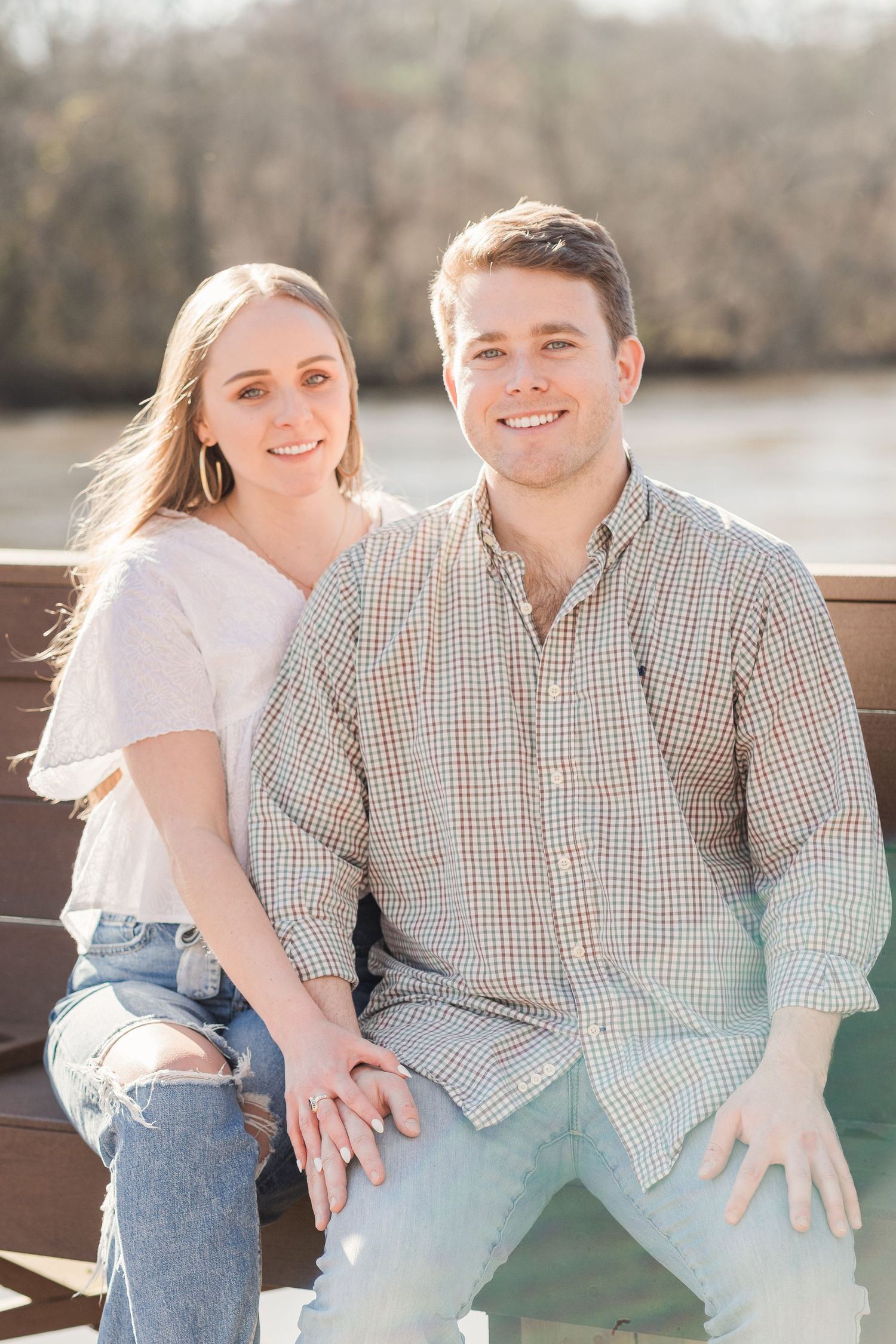 Portrait of couple sitting on bench with the golden hour light and gentle current of the Saluda River behind them.