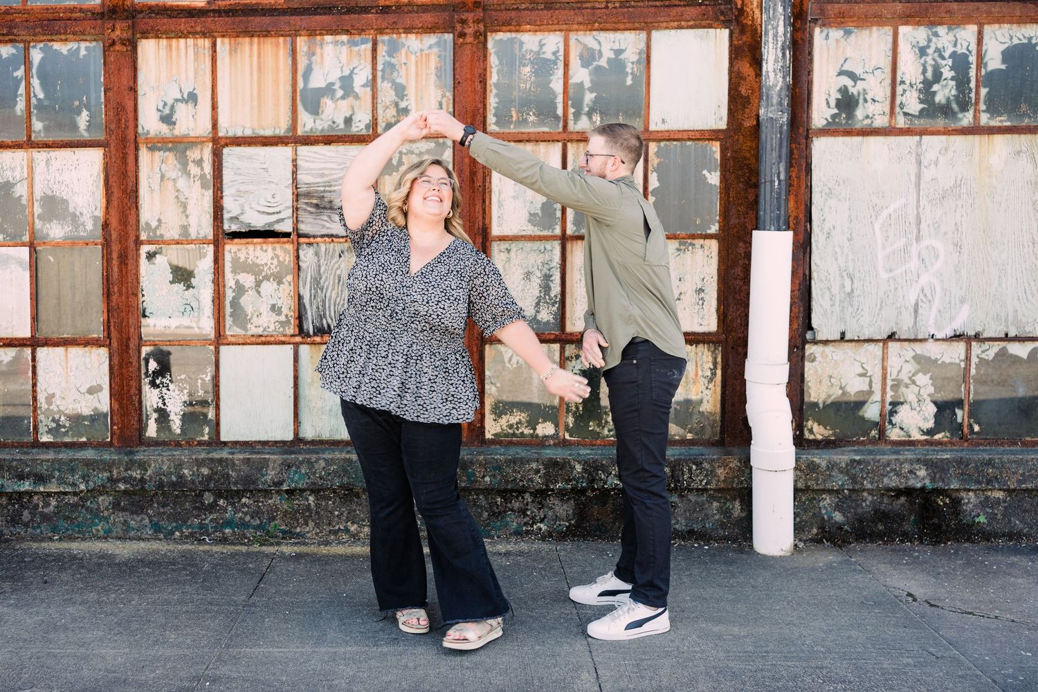 Couple dancing in front of industrial windows at Taylors Mill, laughing together as the man spins the woman.