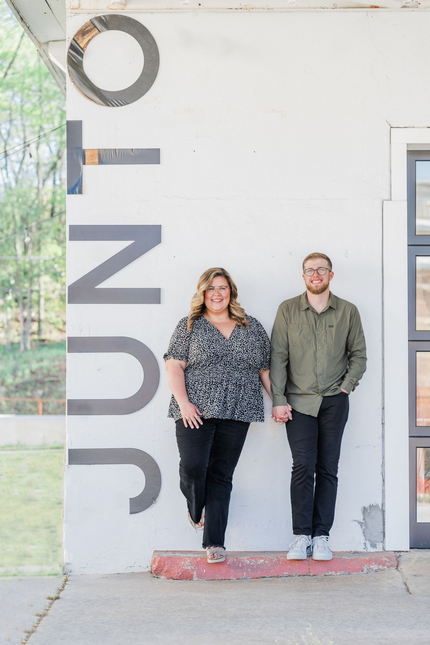 Couple standing in front of Junto coffee shop holding hands and smiling out at the camera