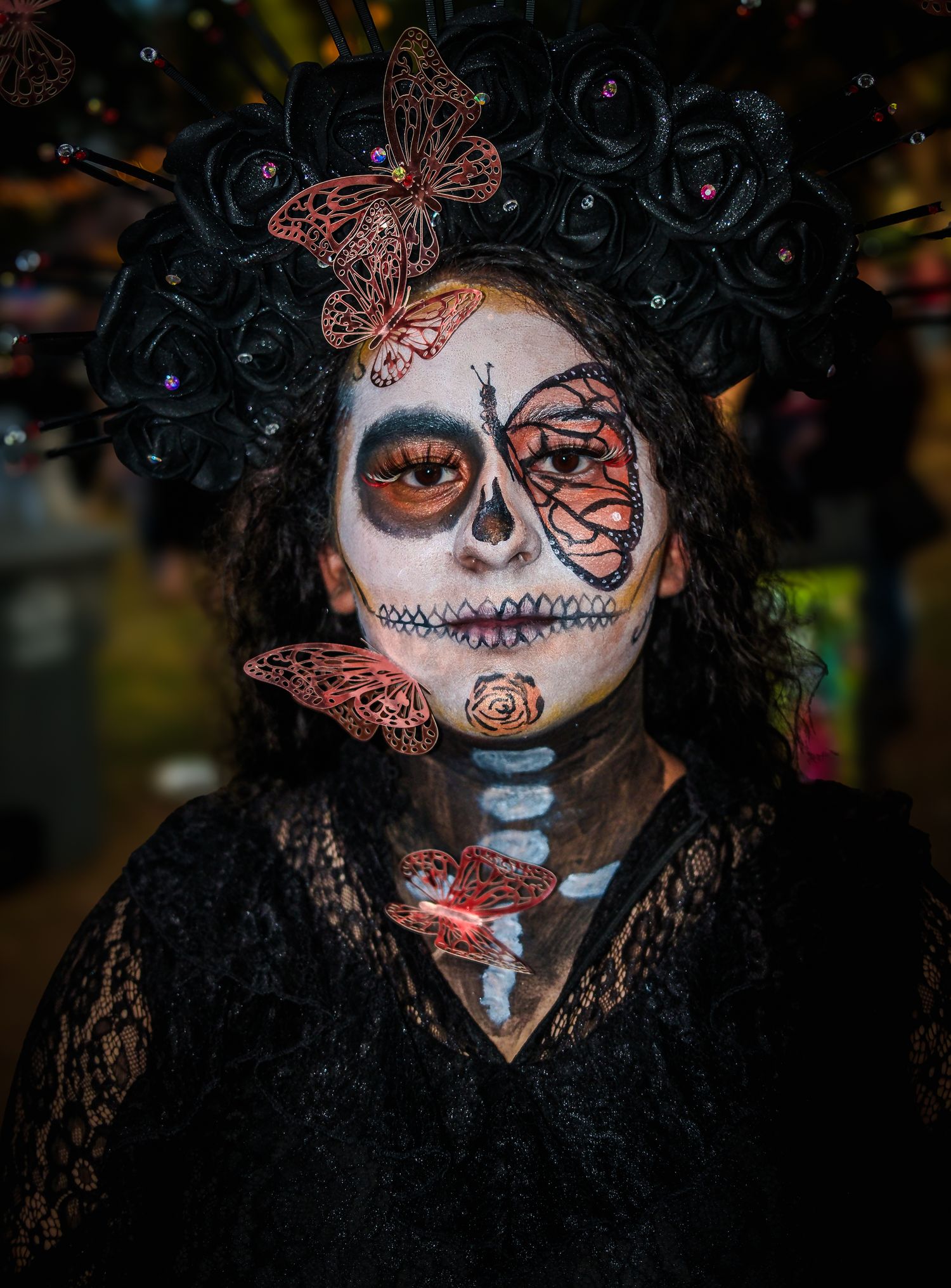 Person wearing intricate Day of the Dead makeup and black lace costume in dramatic lighting.