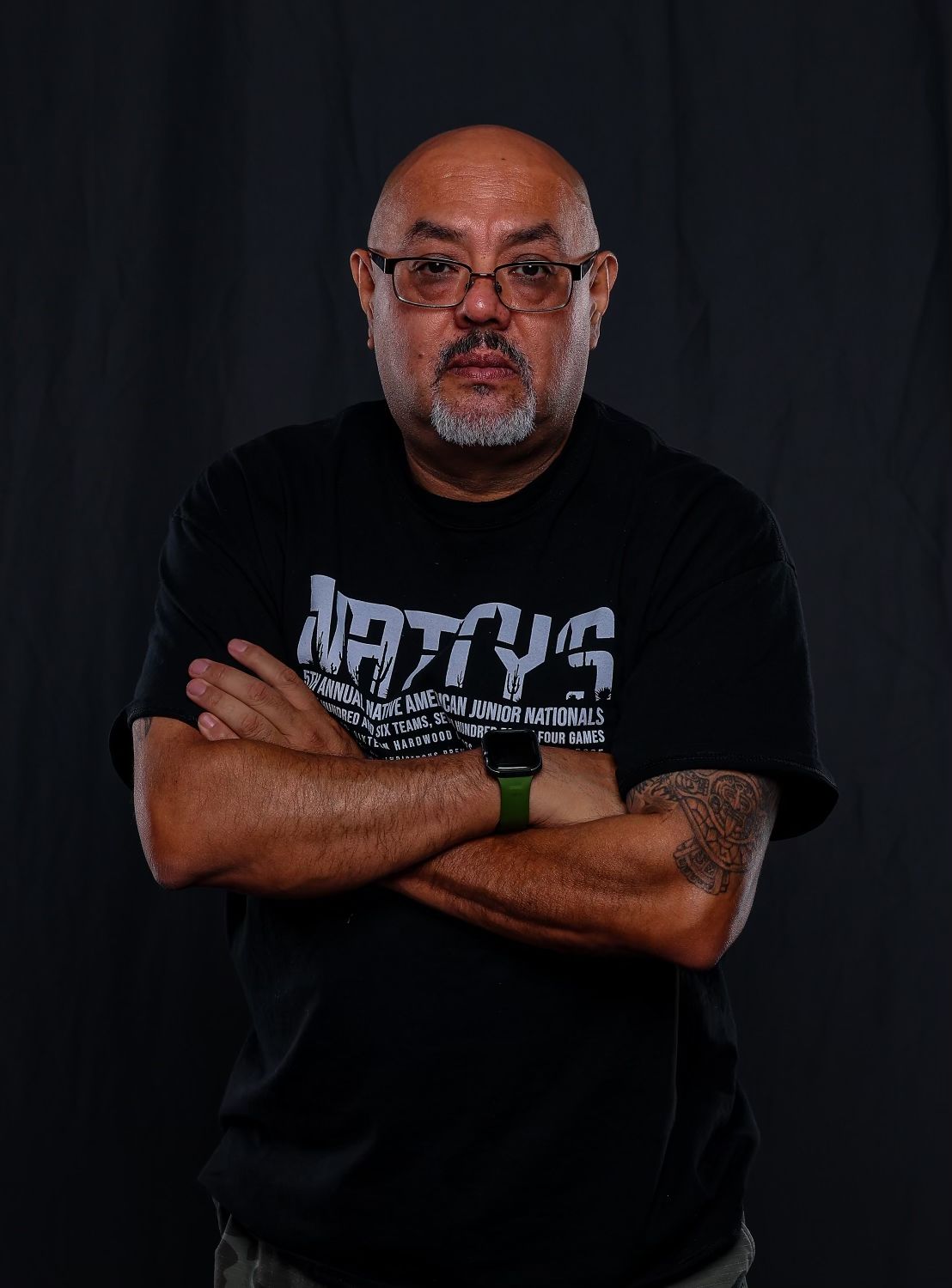 Portrait of person in black t-shirt with crossed arms against dark background.