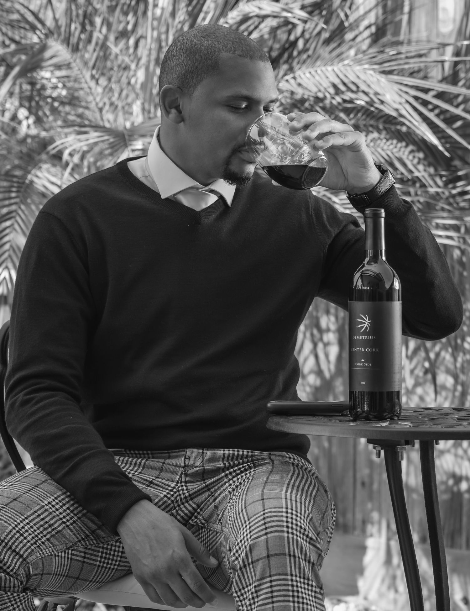 Two people in dark sweaters sitting casually with wine bottles in black and white photo.