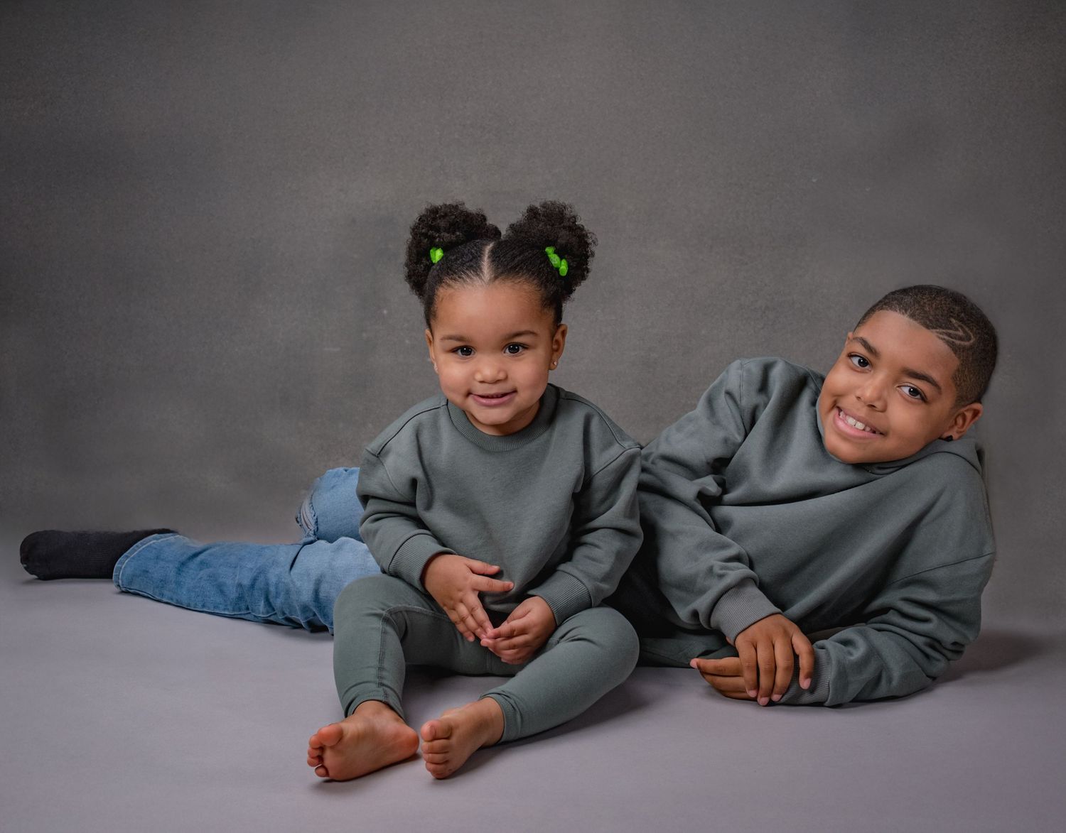 Children in matching grey outfits lying on dark studio backdrop.