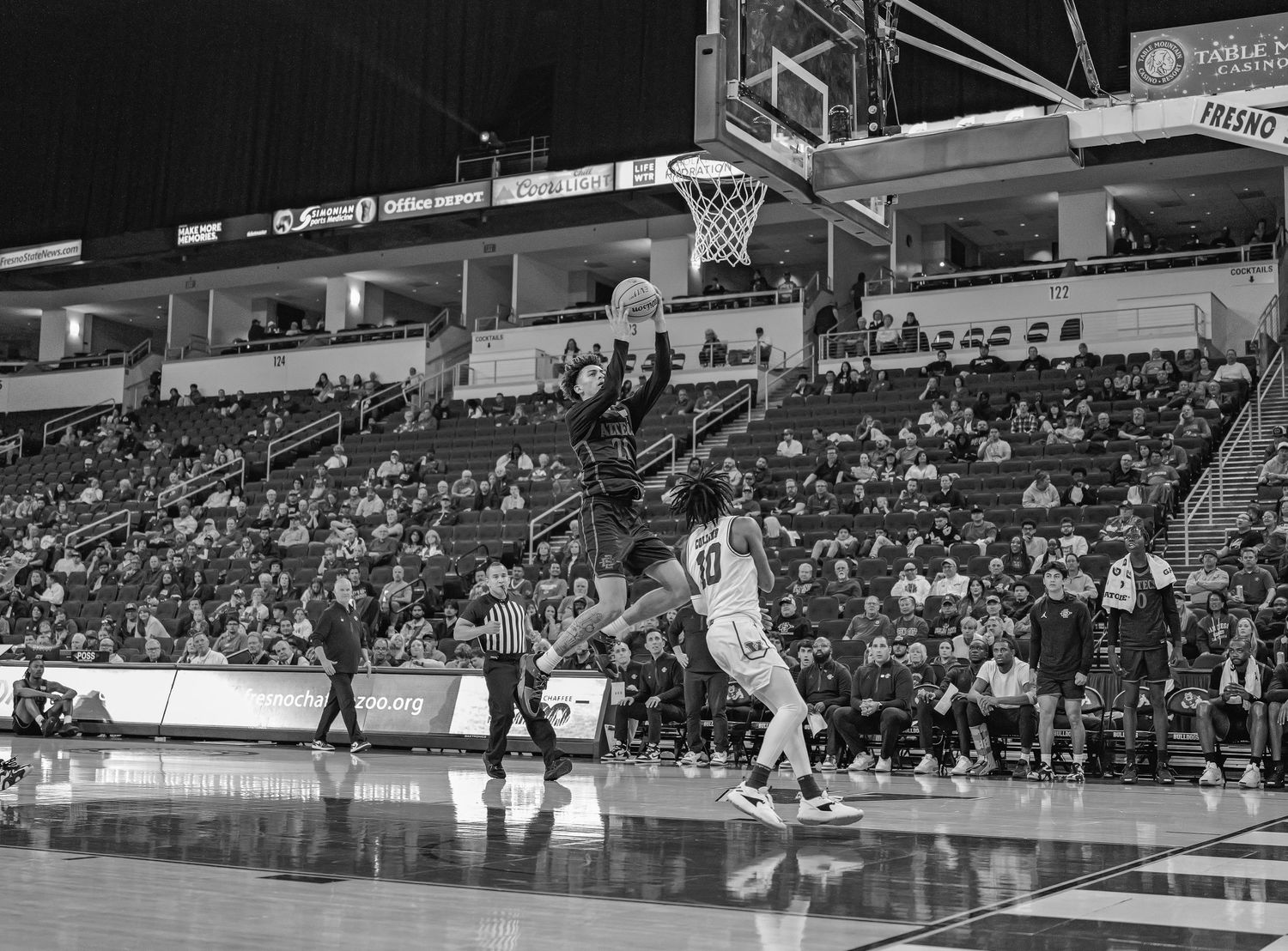 Black and white photo of basketball game showing player making jump shot in arena.