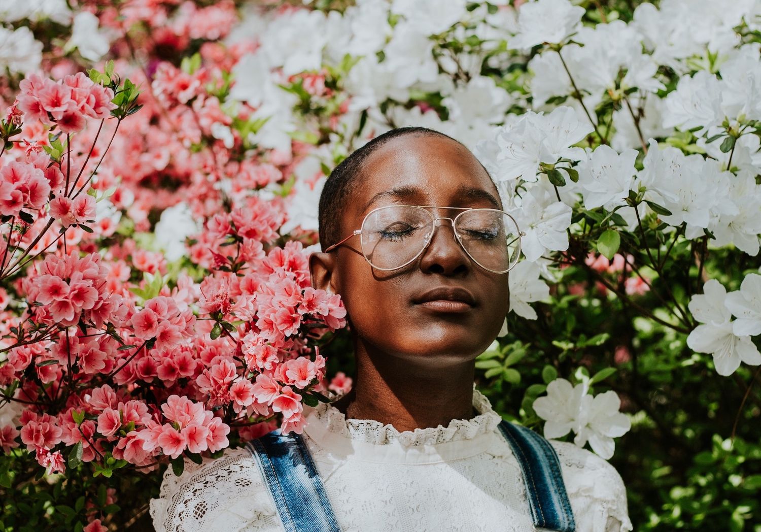 Close-up portrait among pink flowers and greenery in bright natural light.