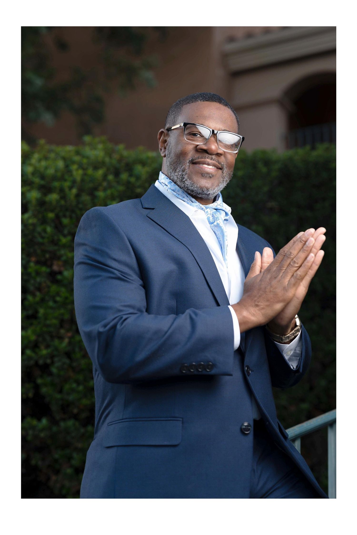 Professional in navy suit and glasses praying or gesturing with hands clasped.