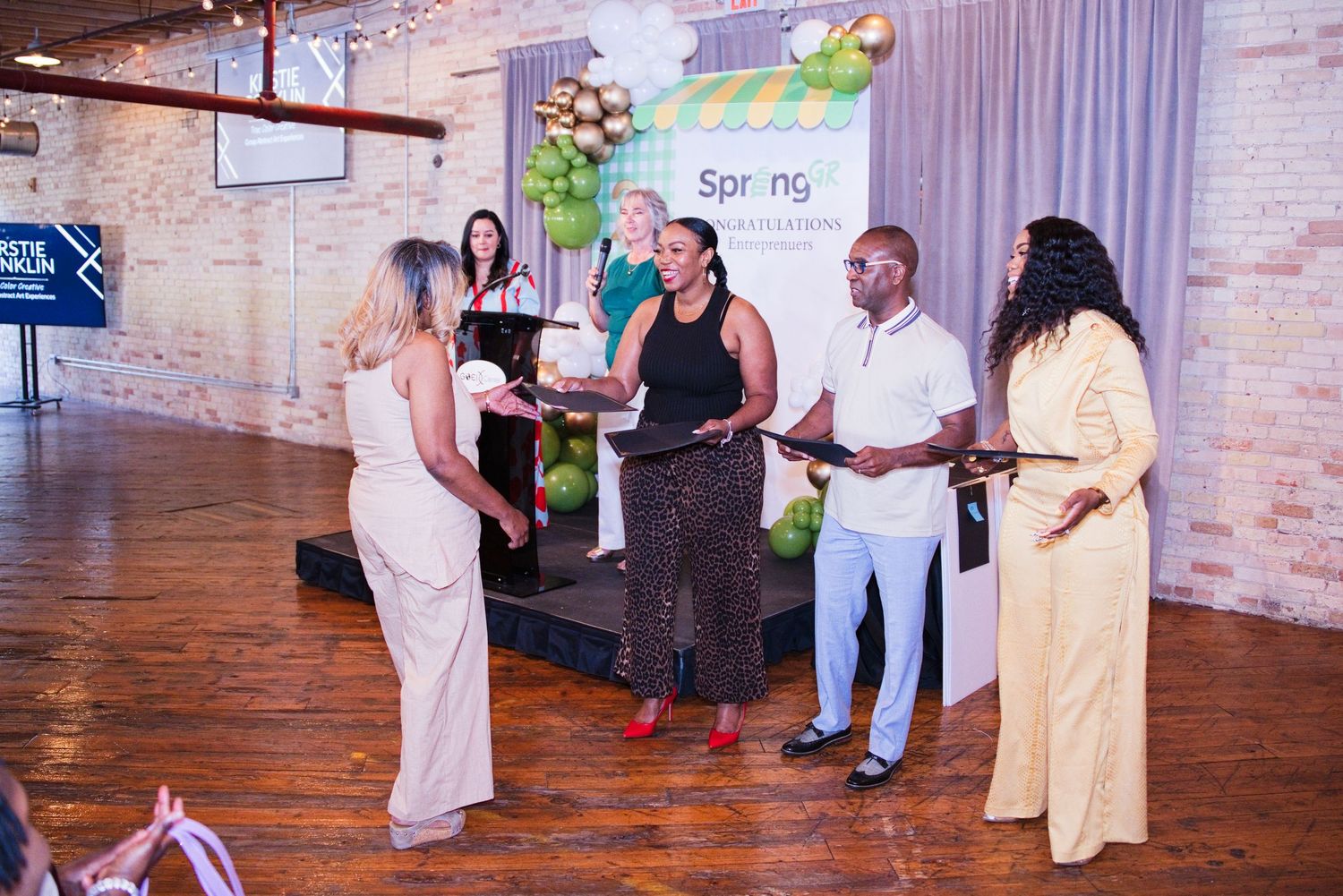 A group of people participate in an award presentation ceremony on stage at a Spring community event.
