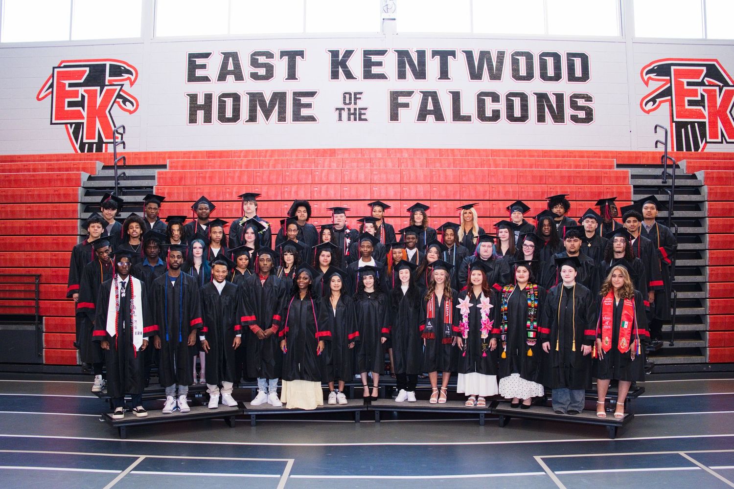 East Kentwood High School Falcons graduates pose in caps and gowns inside the school gymnasium.