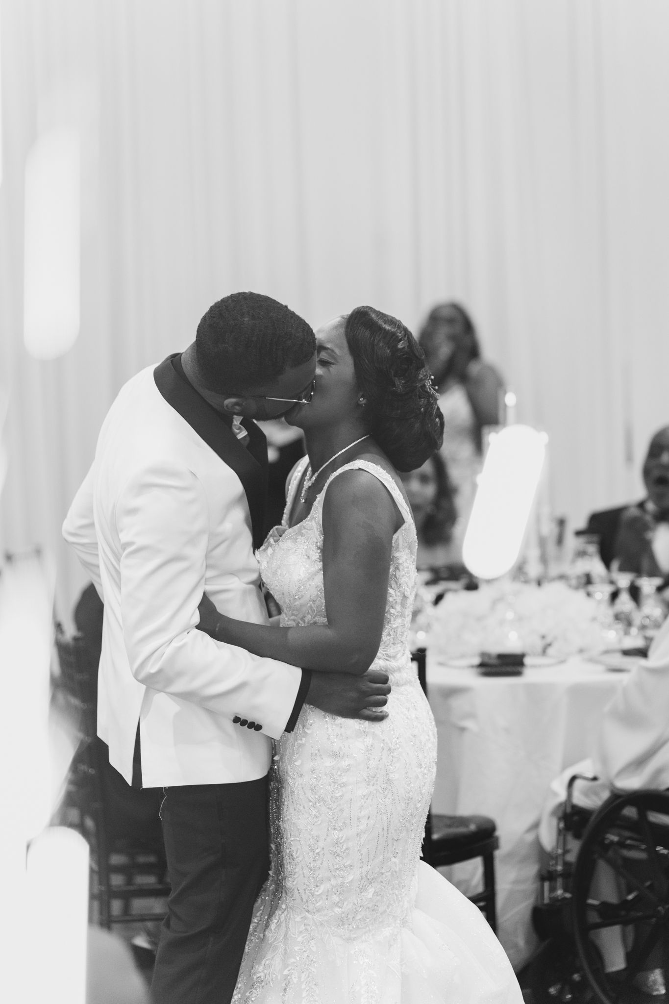Black and white photo of a bride and groom sharing a kiss during their first dance at a wedding reception.