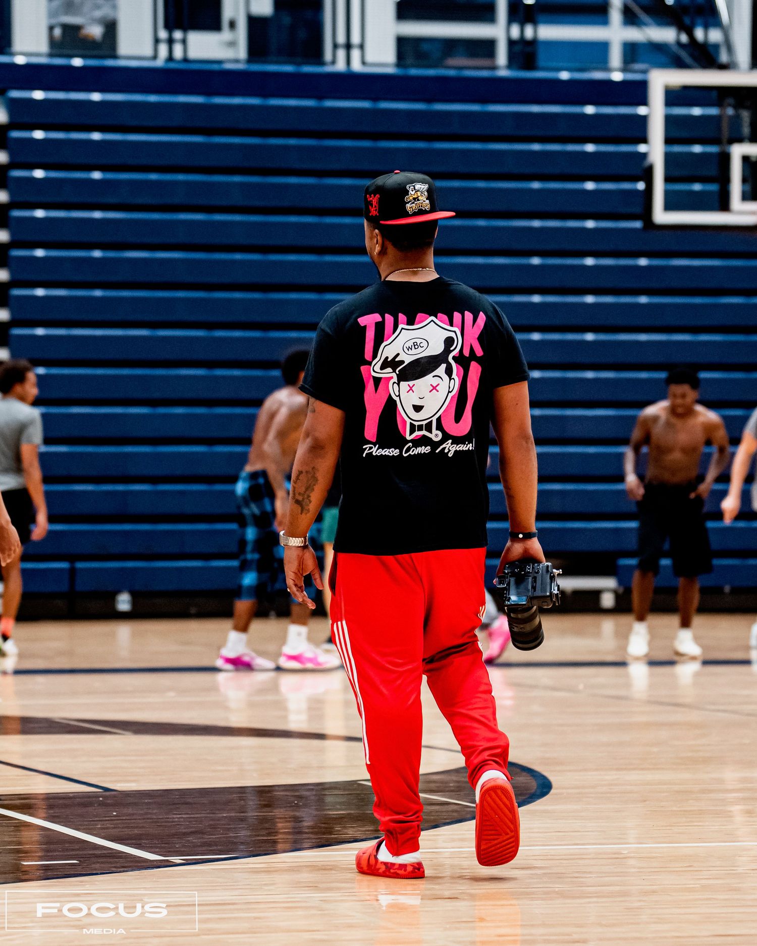 Man in black Thank You graphic tee and red pants walks across indoor basketball court during practice.