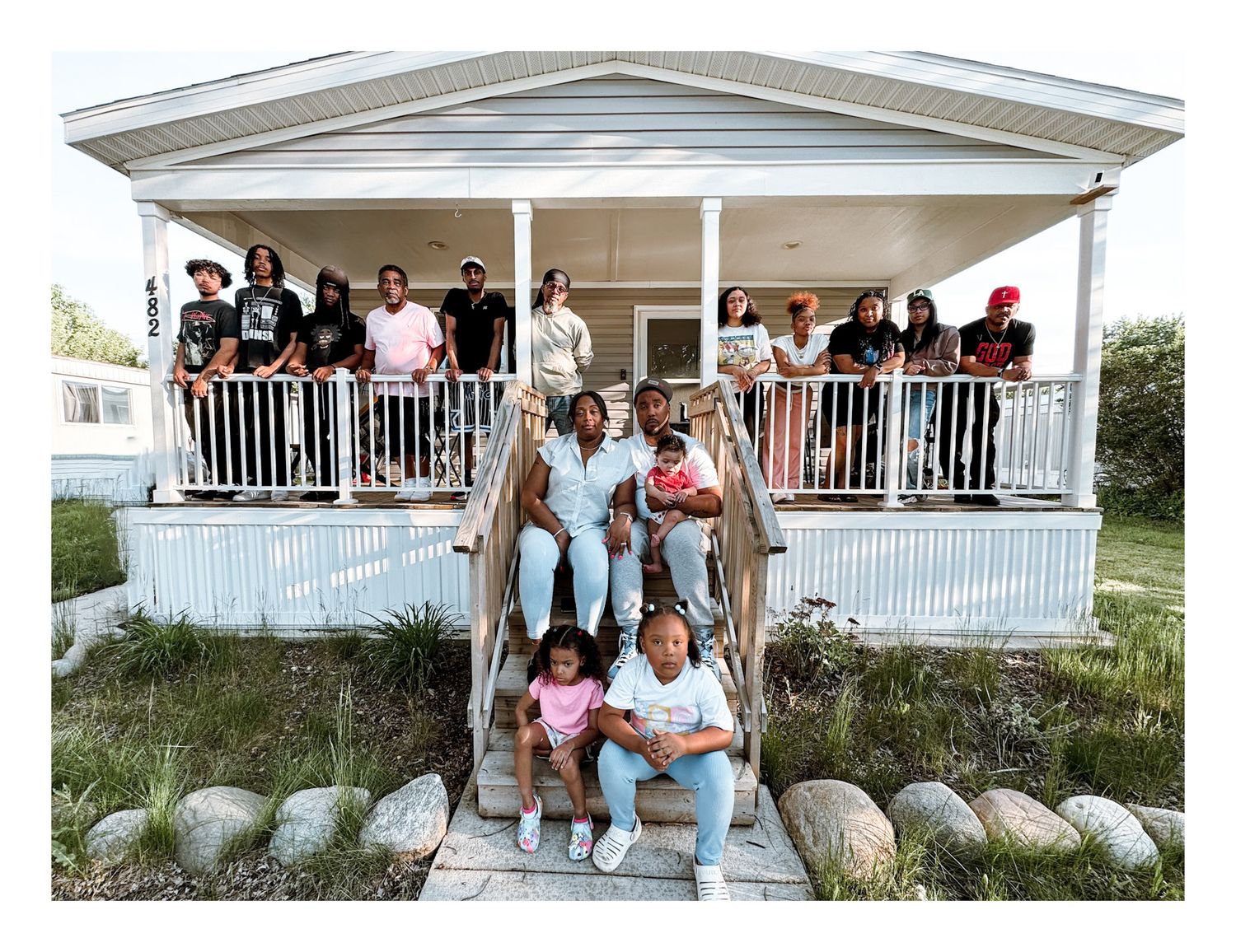 Large family group posing together on porch steps and balcony of a white house for a portrait photo.