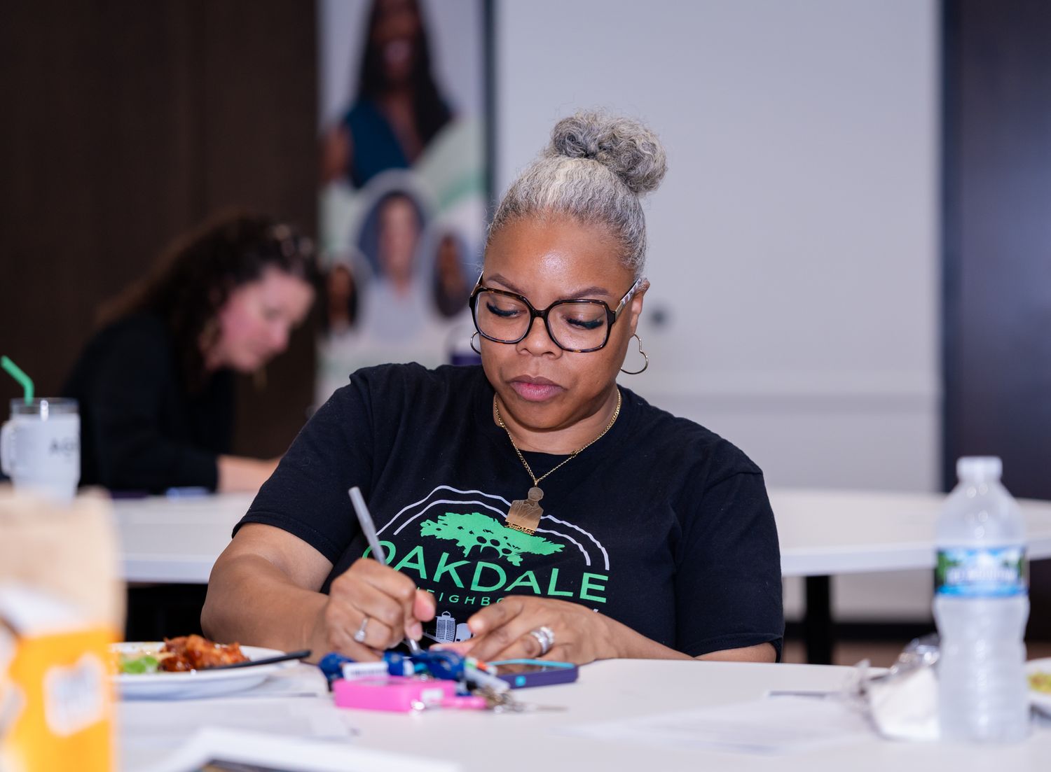 Woman in Oakdale shirt focused on craft activity at workshop table.