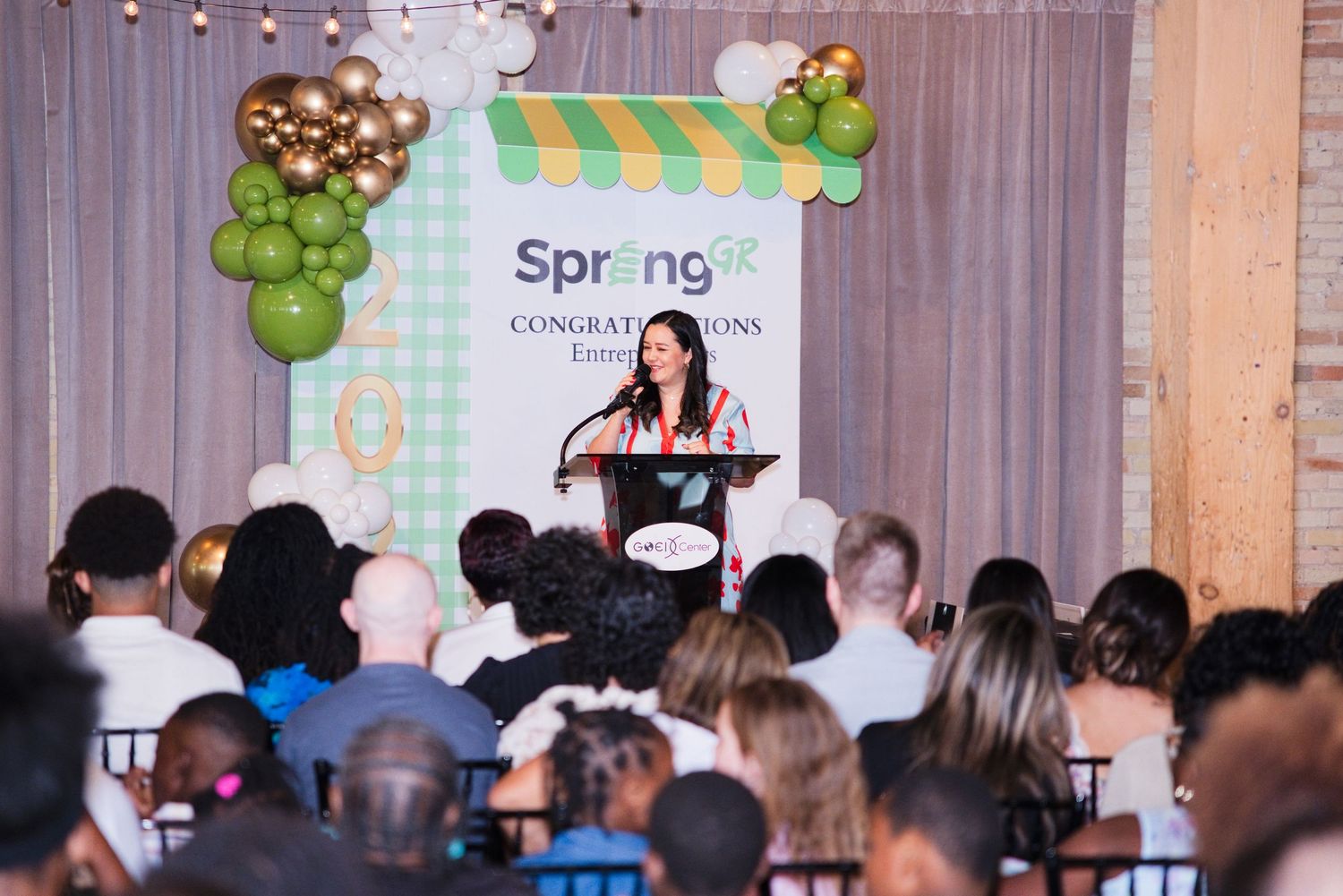 Woman speaking at podium during Spring congratulations awards ceremony with seated audience.