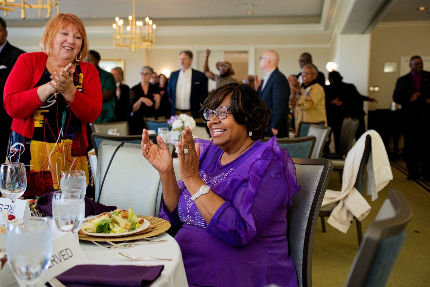 Woman in purple dress clapping joyfully at an elegant banquet celebration event.