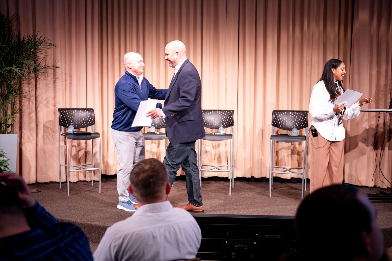 Two men shaking hands on stage during the Amway GROW awards ceremony with a female emcee nearby.