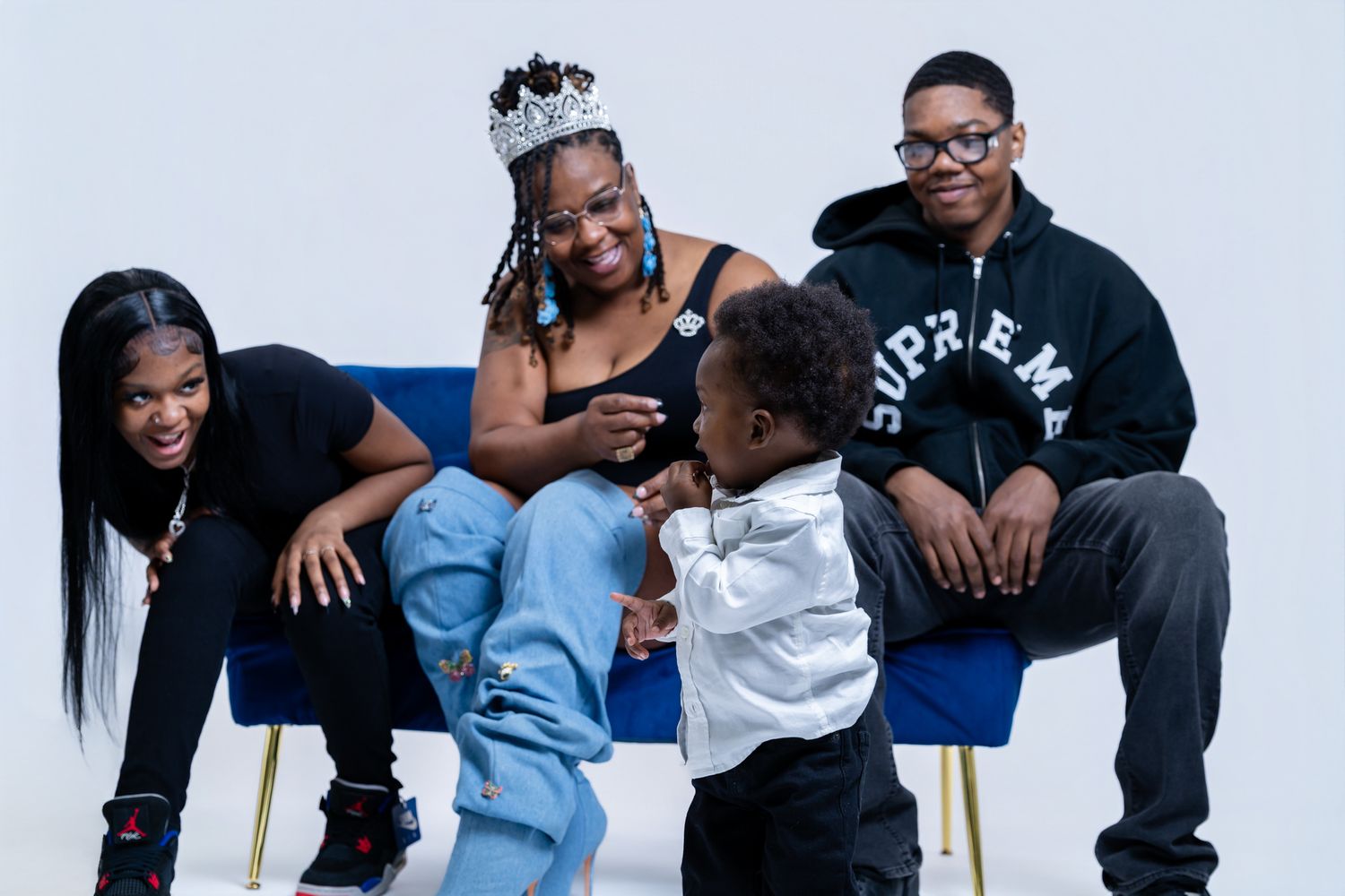 Family portrait with woman wearing crown, three children, and toddler on blue velvet chair.