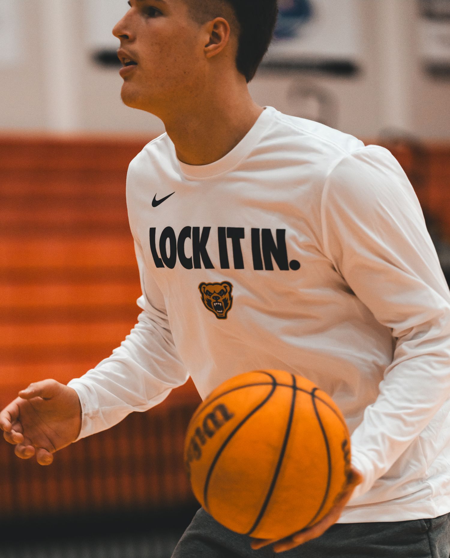 Basketball player dribbling wearing a white Nike 'Lock It In' long sleeve shirt during indoor practice.
