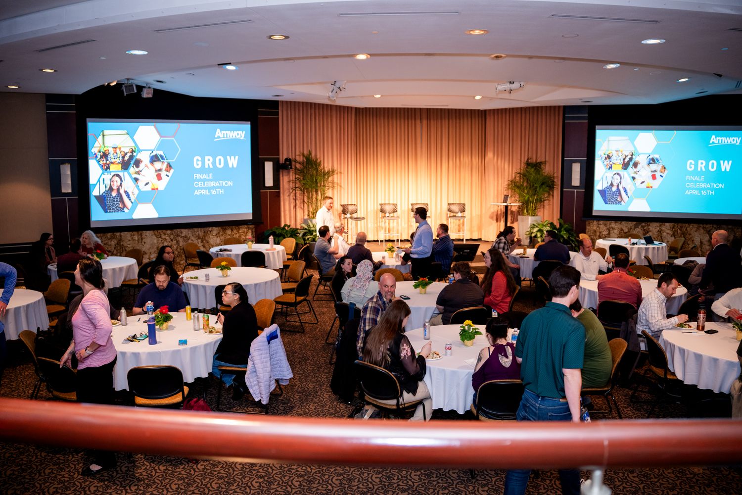 Attendees seated at round tables during the Amway GROW Finale Celebration event with dual projection screens.