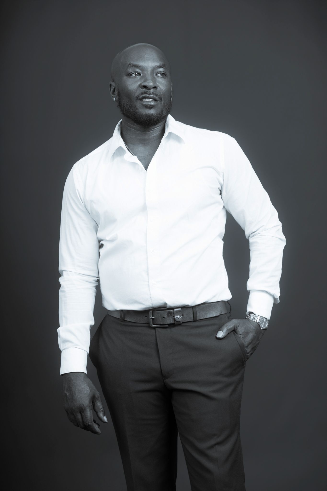 Bald Black man in white dress shirt and black pants poses in black and white portrait.