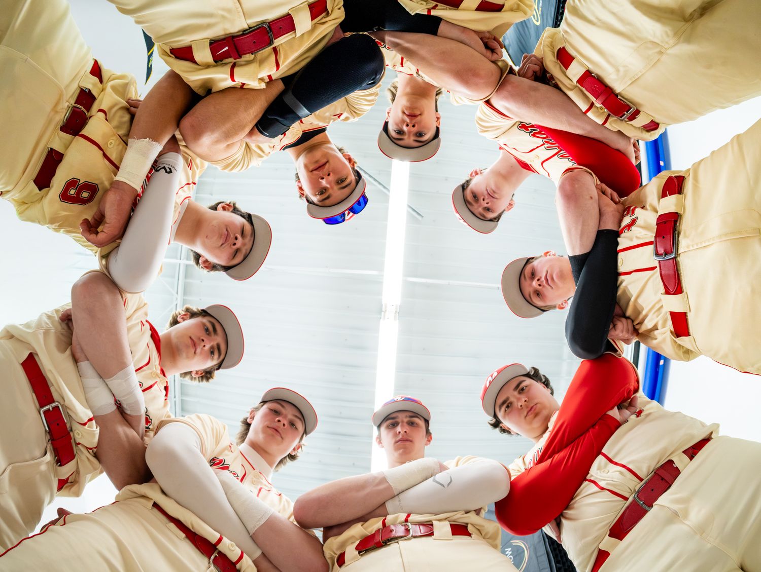 Baseball team huddle photographed from below showing players in cream and red uniforms.