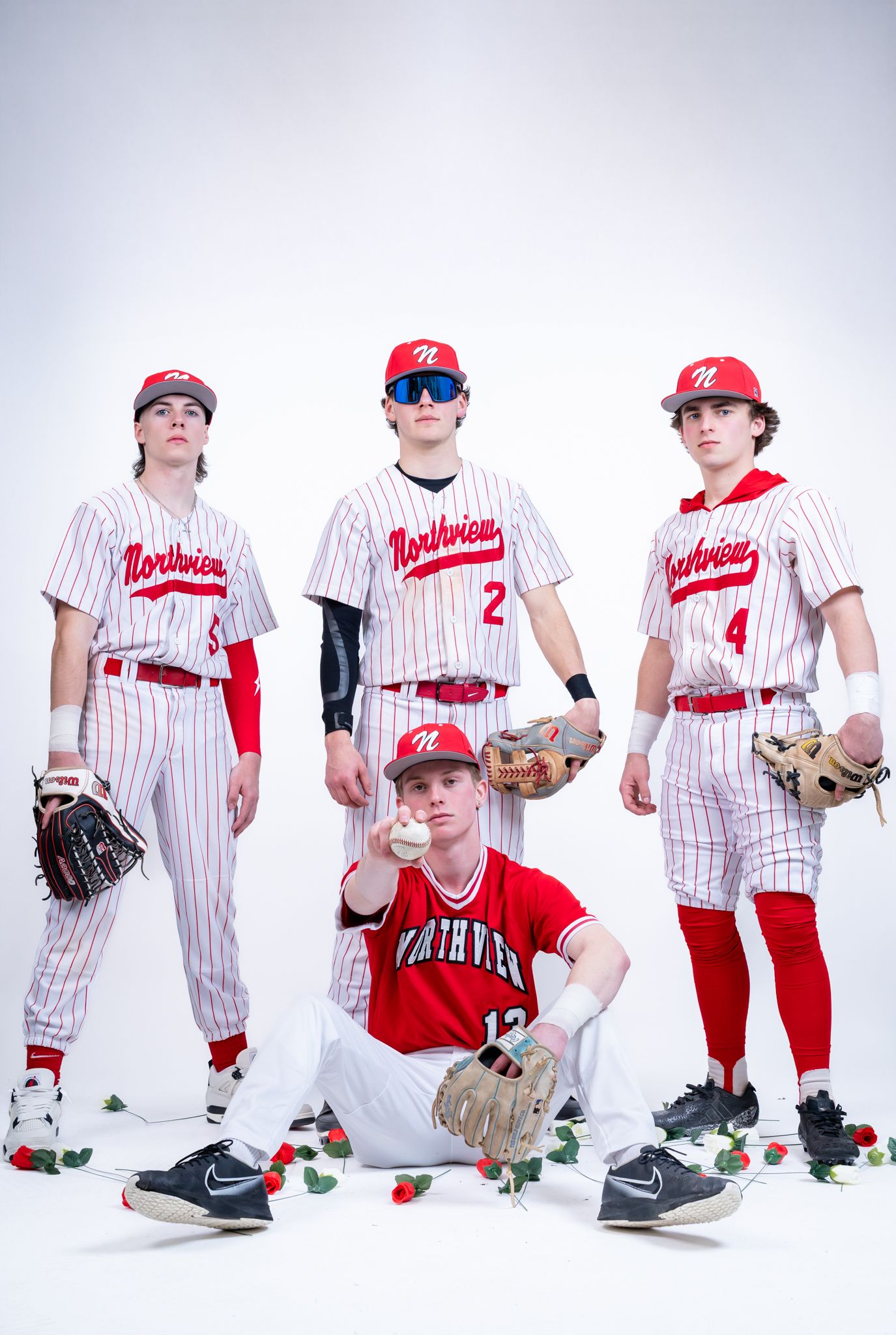 Four Northview high school baseball players pose confidently in red and white uniforms with gloves and roses.